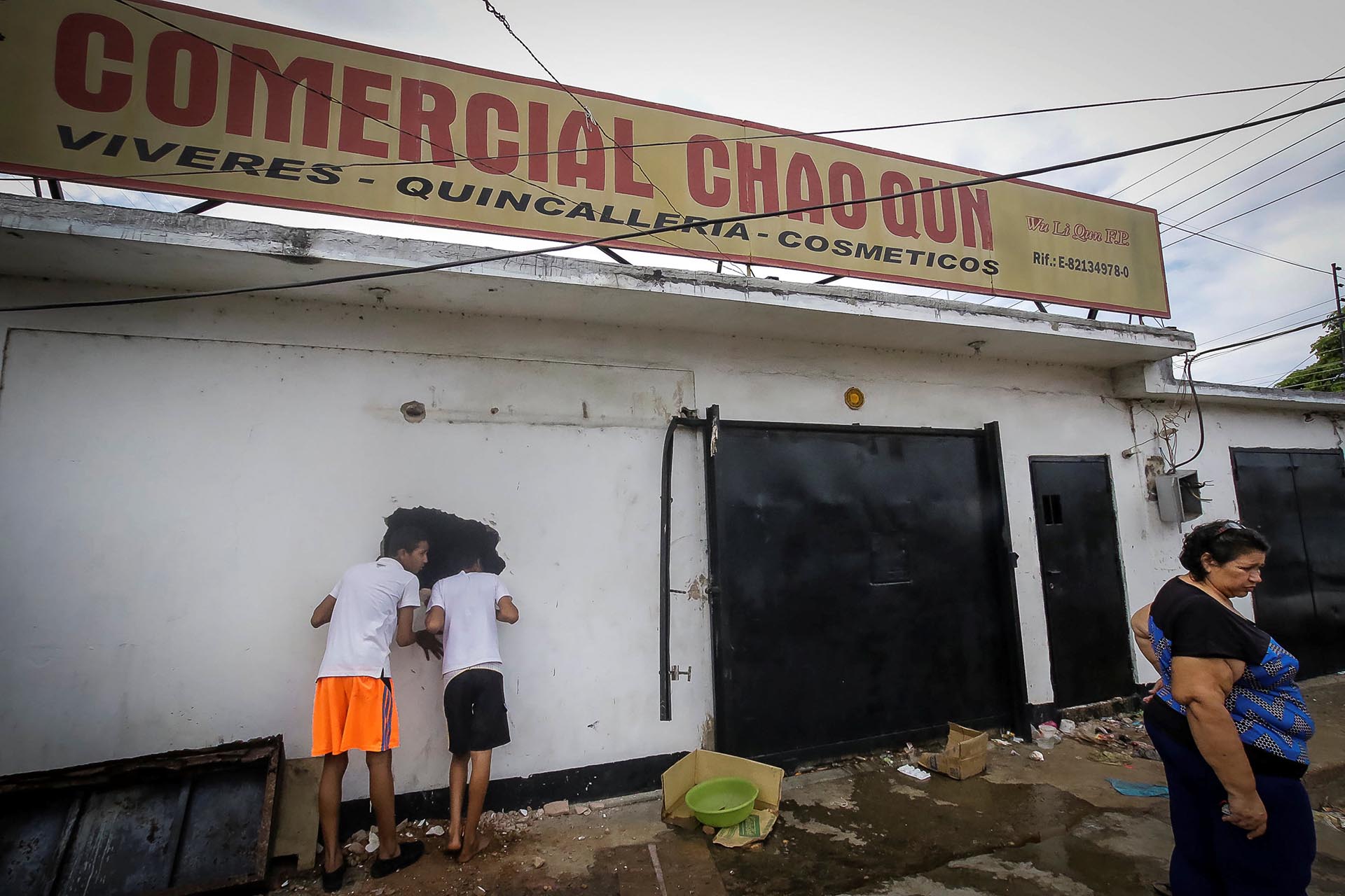 Jóvenes miran por el hueco en la pared de un supermercado saqueado en Ciudad Bolívar