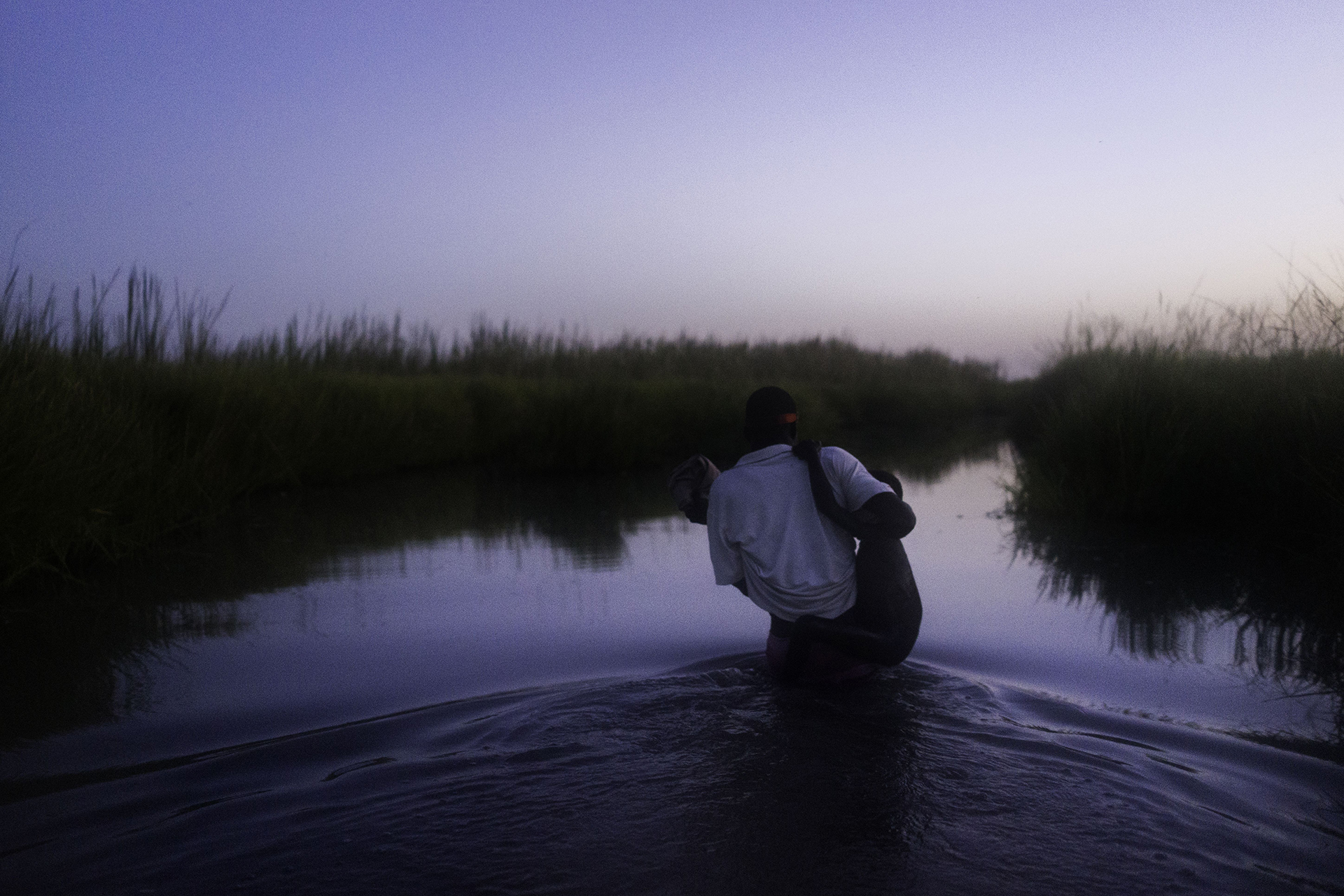ISLA DE KOK, SUDÁN DEL SUR: Al atardecer, caminando a través de los pantanos del Estado de Unidad, un integrante de MSF carga a un niño mientras su familia se abre camino hacia la relativa seguridad de la isla de Kok, en donde más de 2000 personas se están refugiando del conflicto (©Dominic Nahr)