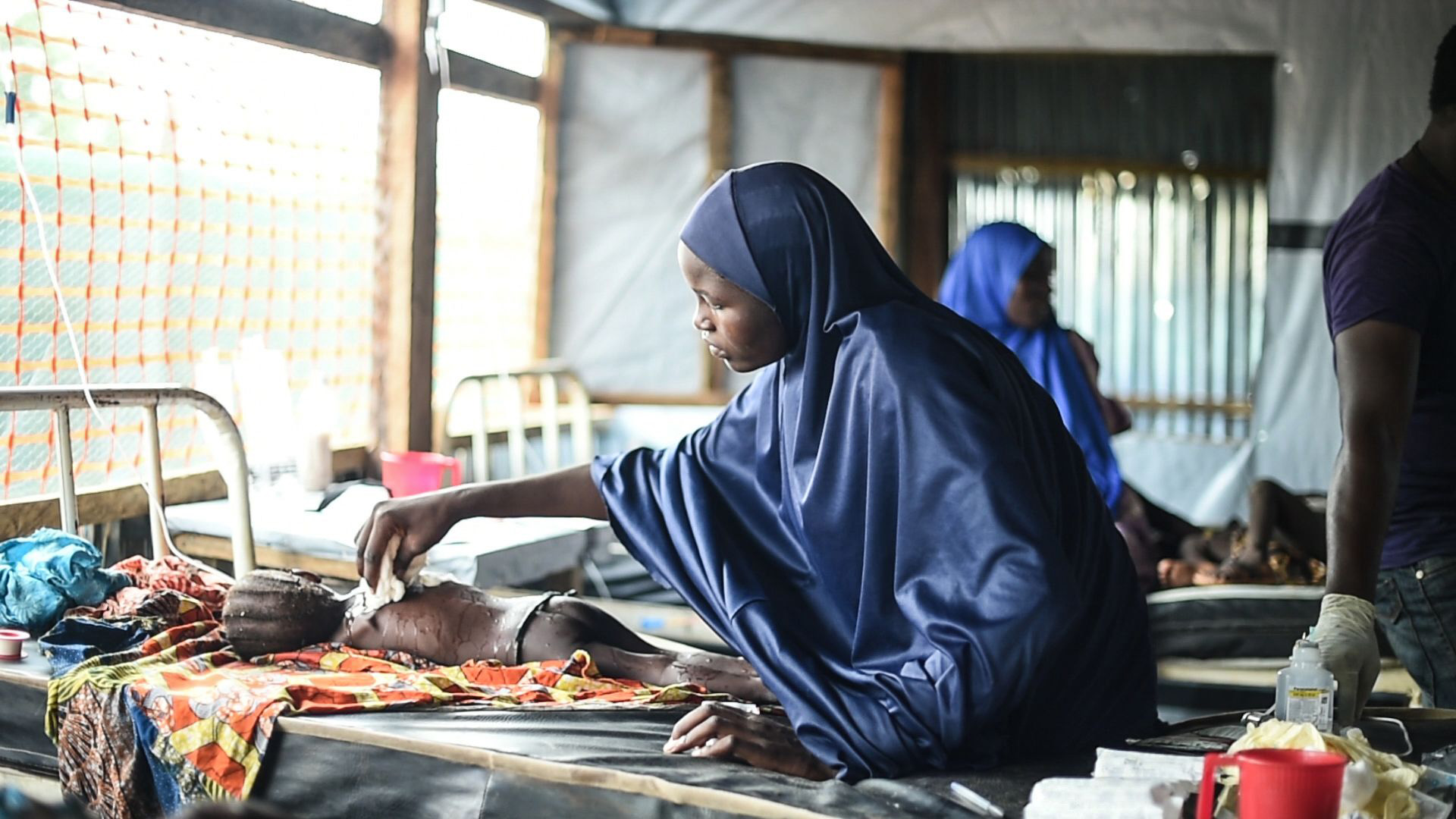 ESTADO DE BORNO, NIGERIA: Una madre colocando un trapo húmedo en el cuerpo de su hija para intentar bajar la fiebre en la sala de aislamiento del hospital general en Damboa, en el estado de Borno, en Nigeria. Su hija está siendo atendida por un sarampión con complicaciones. Los casos más severos son referidos al hospital en Biu, a dos horas de camino en auto (©Ikram N’gadi)