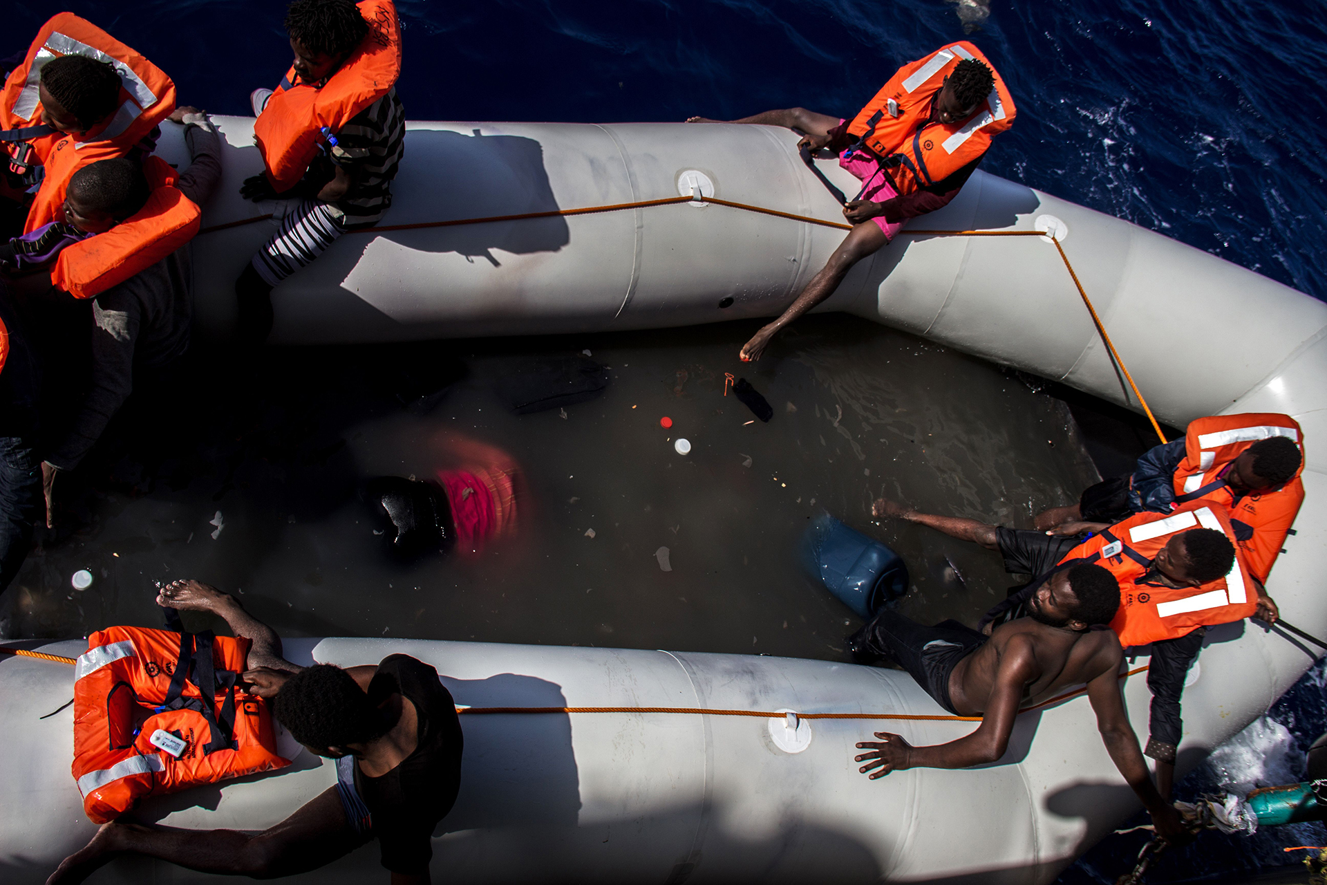 BÚSQUEDA Y RESCATE EN EL MEDITERRÁNEO: Un grupo de personas esperando ser rescatadas de un bote; junto a ellos están los cuerpos de quienes murieron intentando cruzar el mar Mediterráneo. Los equipos de MSF salvaron a 246 personas y encontraron 25 cuerpos sin vida en el bote (© Borja Ruiz Rodriguez)