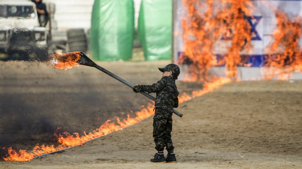 Un niño palestino enciende fuego a una bandera de Israel en el acto final del evento de graduación (AFP)