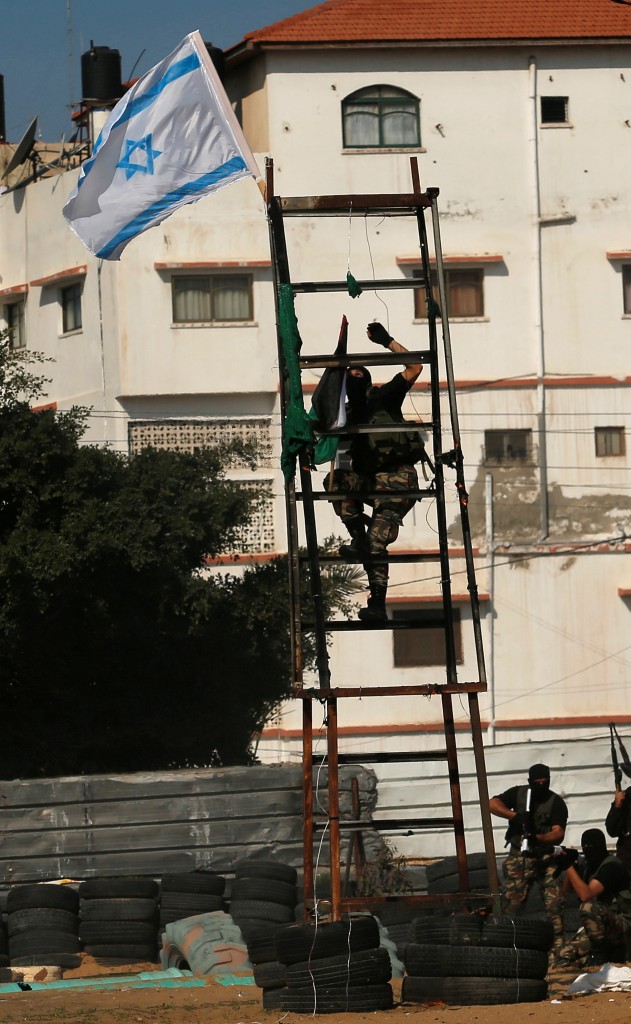 Un miembro de Hamas busca retirar la bandera de Israel y reemplazarla con la de Palestina, señal de la “captura” de la posición del ejército israelí (AFP)