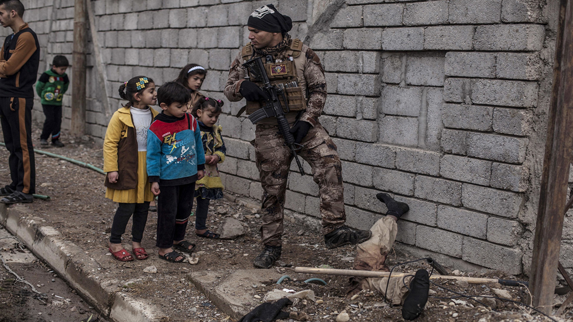 La brutalidad de la guerra: niños observan el cuerpo semienterrado de un militante del ISIS, ante la mirada de un soldado iraquí (AP)