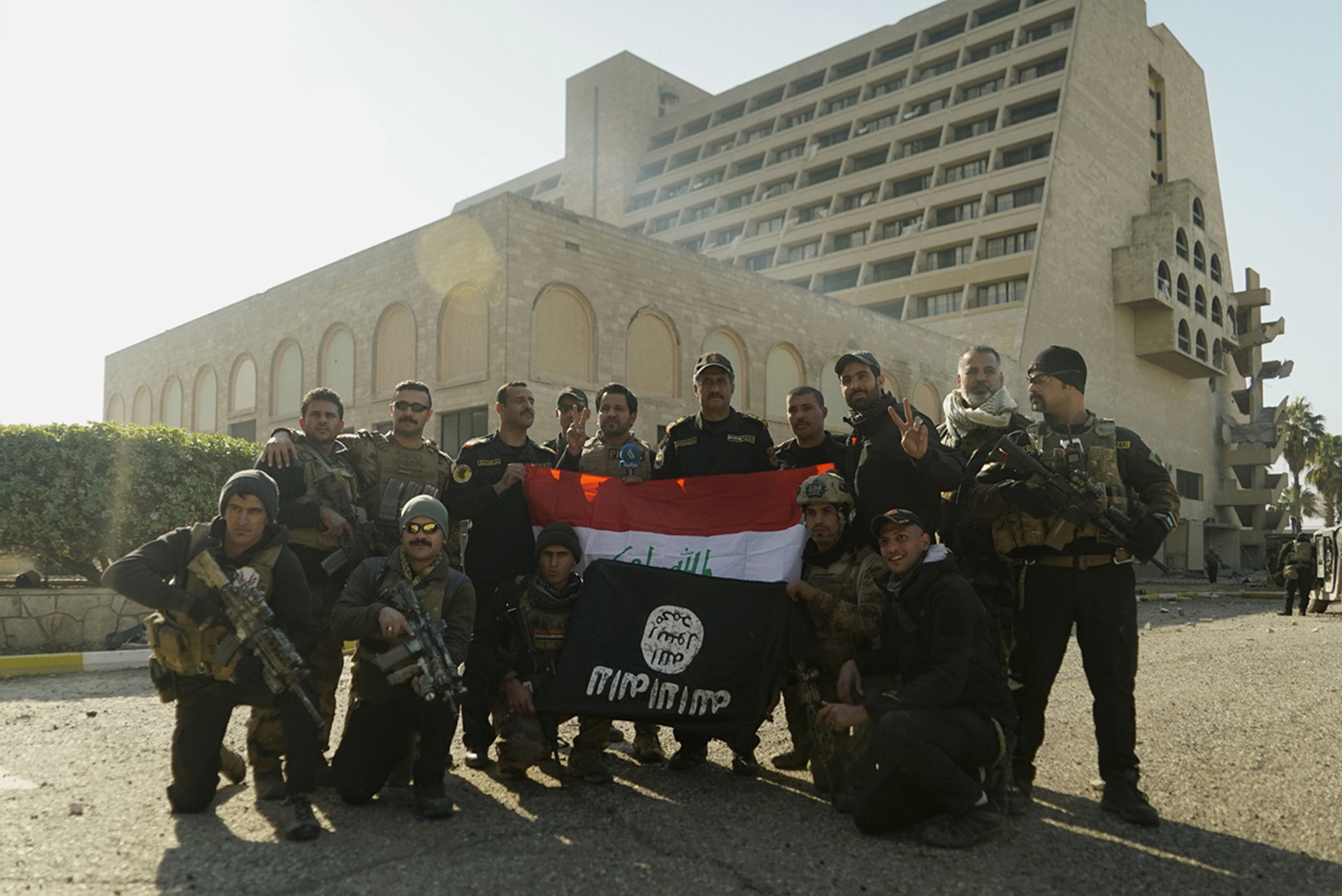 Tropas especiales posan con la bandera iraquí y una enseña del ISIS capturada, frente al Hotel Nineveh, otro objetivo preciado en esta primera parte de la ofensiva (AP)