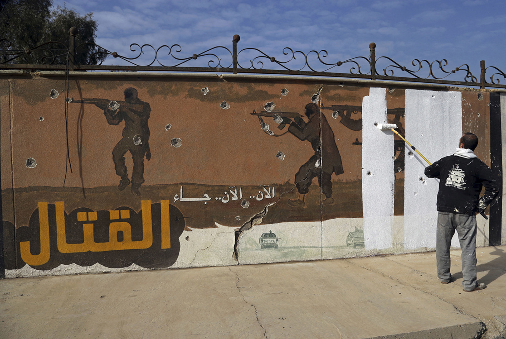Un voluntario cubre con pintura un mural propagandístico del ISIS en el este de Mosul que dice “Ahora comienza la lucha” (AP)