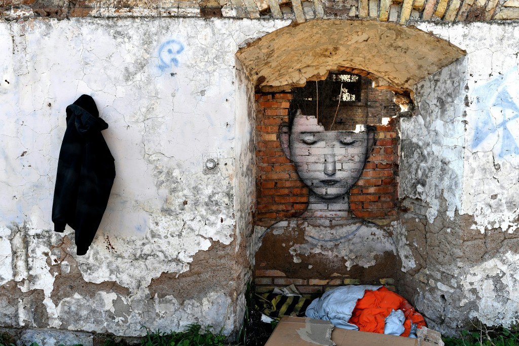 Un migrante se instaló a los pies de la pintura de un niño, afectada por el clima (AFP/ Alberto Pizzoli)