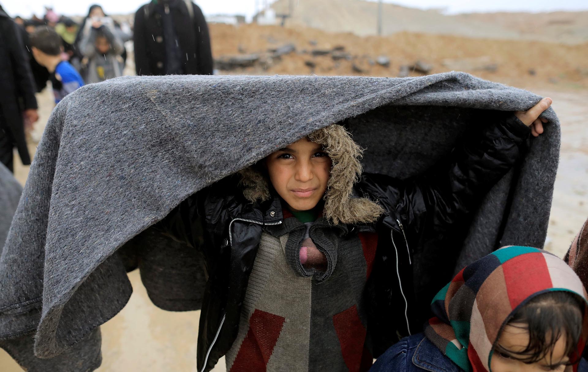 Una niña iraquí se tapa con una manta de la lluvia en plena huida
