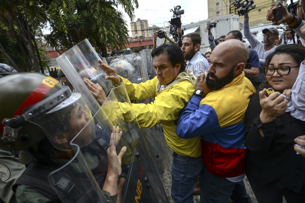 Venezuelan opposition deputies Carlos Paparoni (C) and Marco Bozo (R) scuffle with National Guard personnel in riot gear during a protest in front of the Supreme Court in Caracas on March 30, 2017. Venezuela's Supreme Court took over legislative powers Thursday from the opposition-majority National Assembly, whose speaker accused leftist President Nicolas Maduro of staging a "coup." / AFP PHOTO / JUAN BARRETO / 