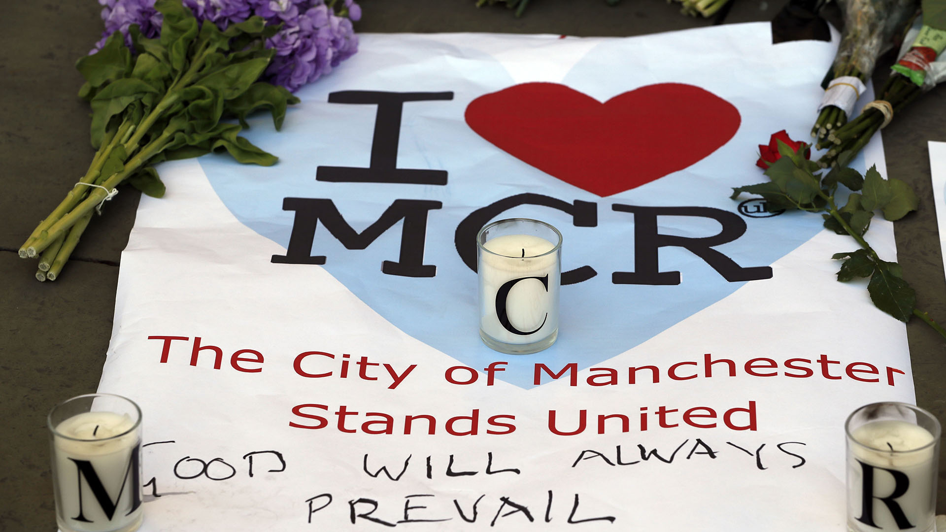 “La ciudad de Manchester permanece unida”, se puede leer en una bandera tendida sobre el piso con flores y velas (AP)