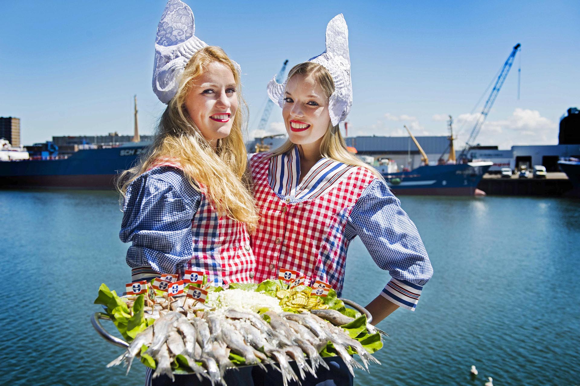 Dos mujeres vestidas al estilo tradicional de Holanda posan con arenques en el puerto de Scheveningen. El primer barril de arenques ha salido a subasta por 65.000 euros donados a caridad