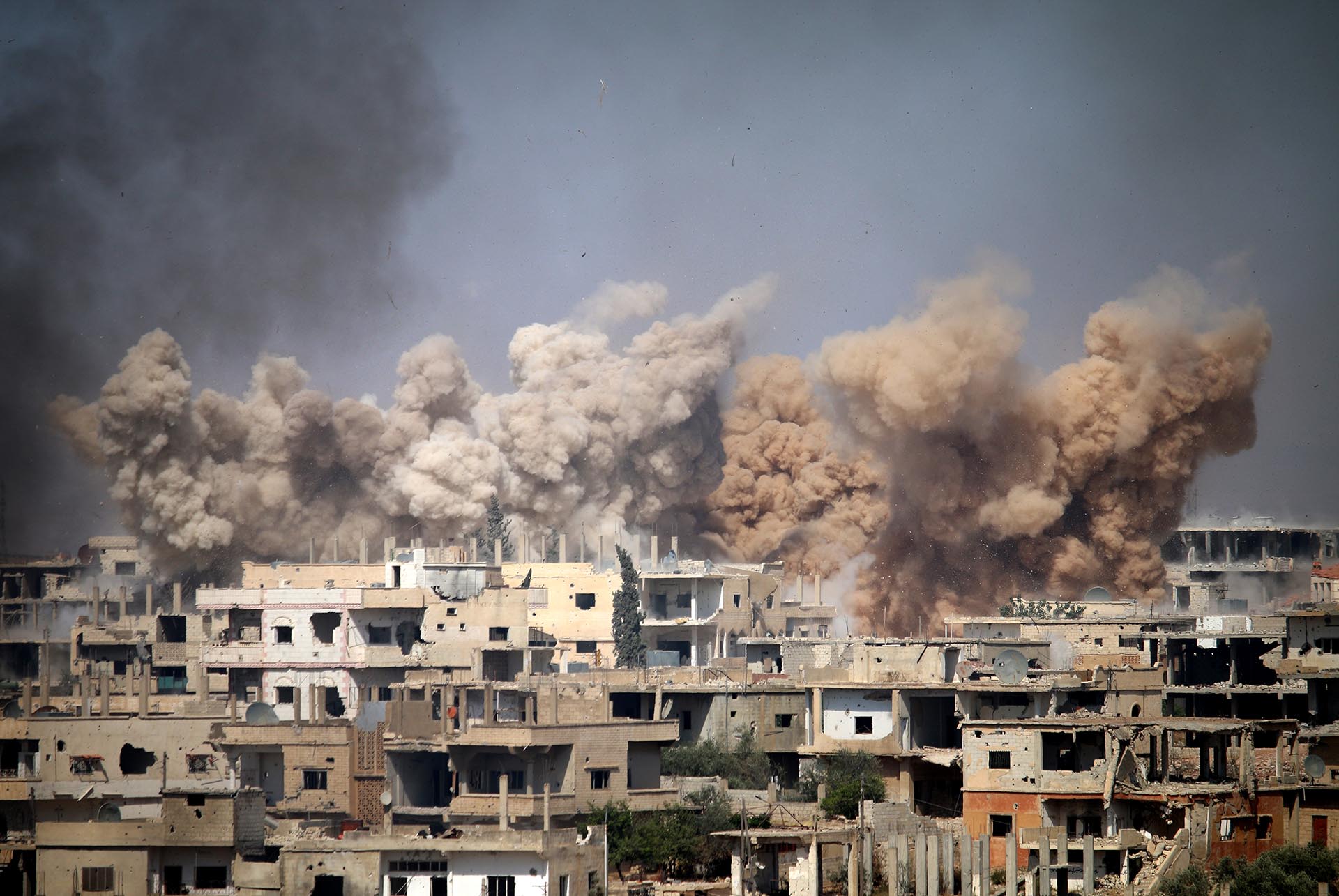 El humo entre los edificios después de un ataque aéreo en una área controlada por los rebeldes en la ciudad siria de Daraa