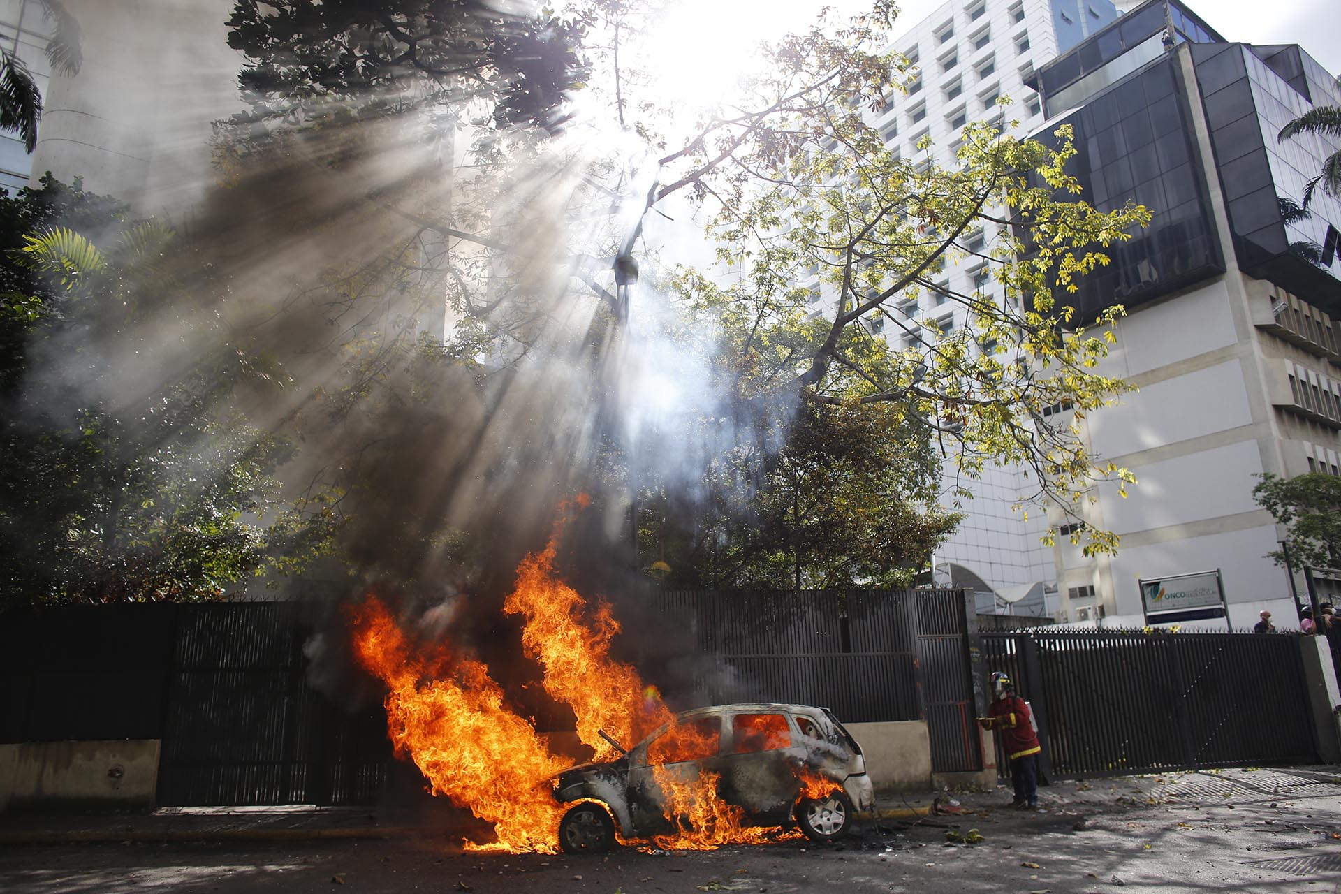 Un bombero apaga el fuego de un coche incendiado durante la represión a las protestas en Caracas, Venezuela