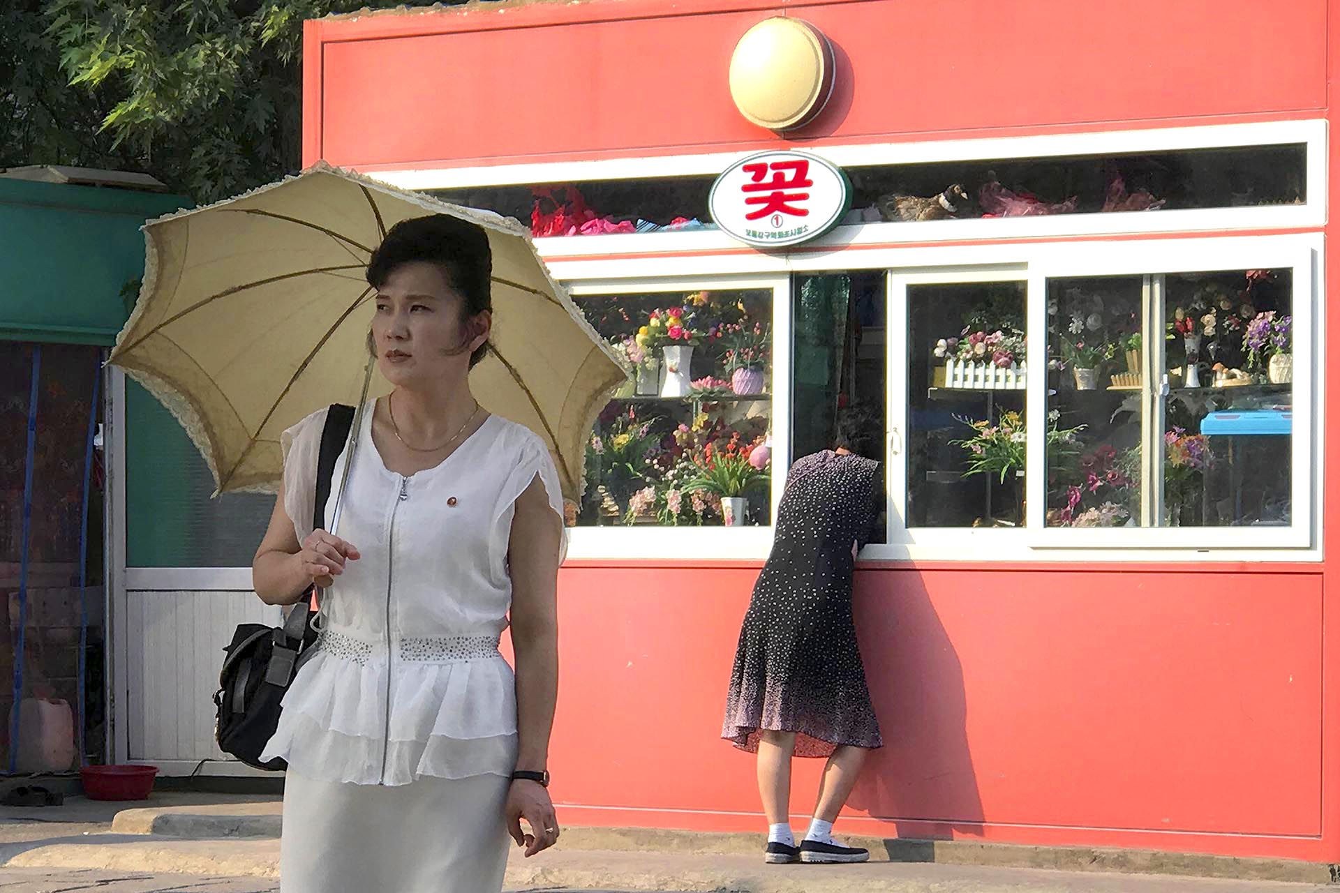 Una mujer se detiene en un quiosco que vende regalos y flores en Pyongyang, Corea del Norte, mientras otra espera a cruzar la calle