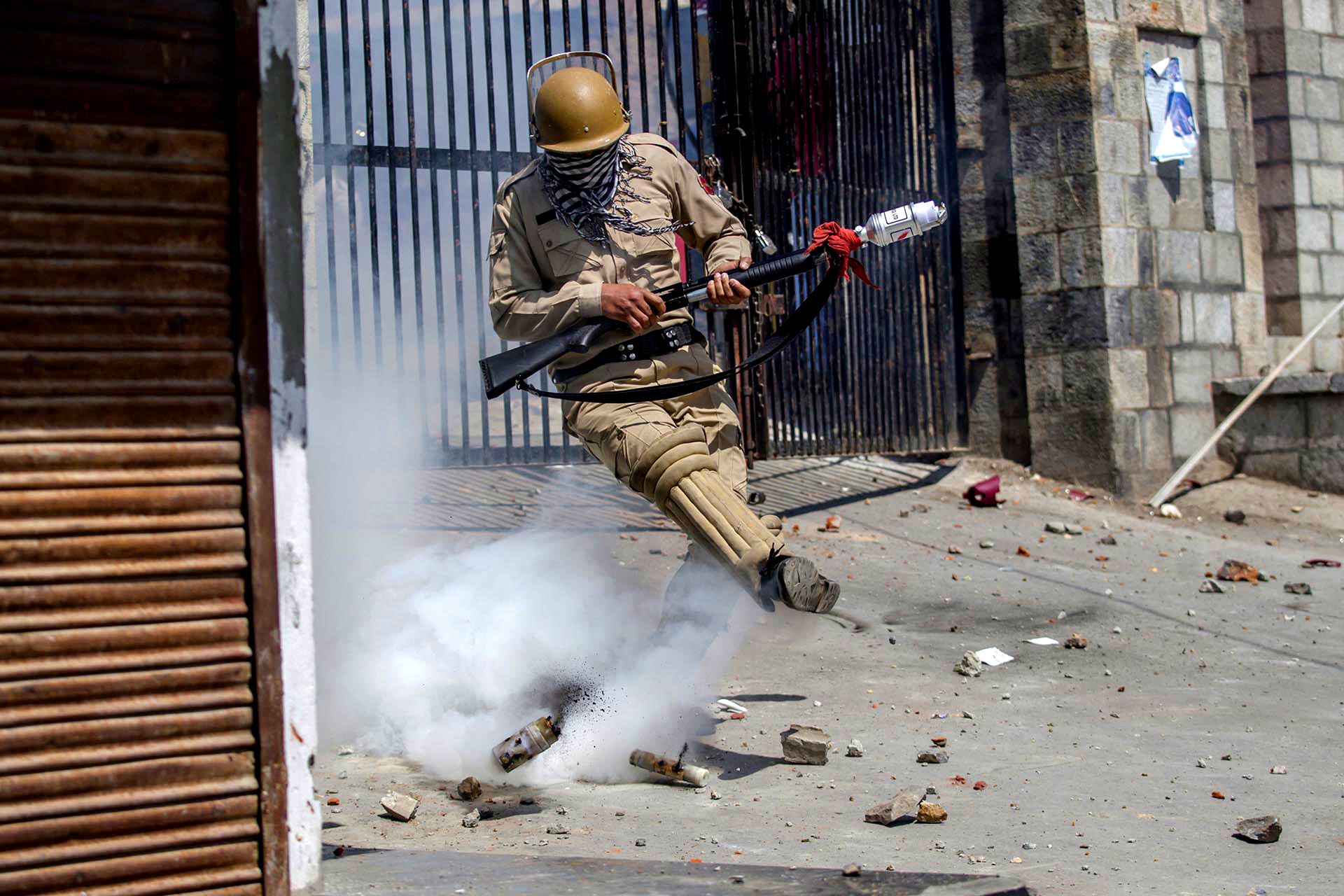 Un policía indio patea un proyectil de gas lacrimógeno en un intento de arrojarlo hacia los manifestantes en Srinagar, en el valle de Cachemira, controlado por la India