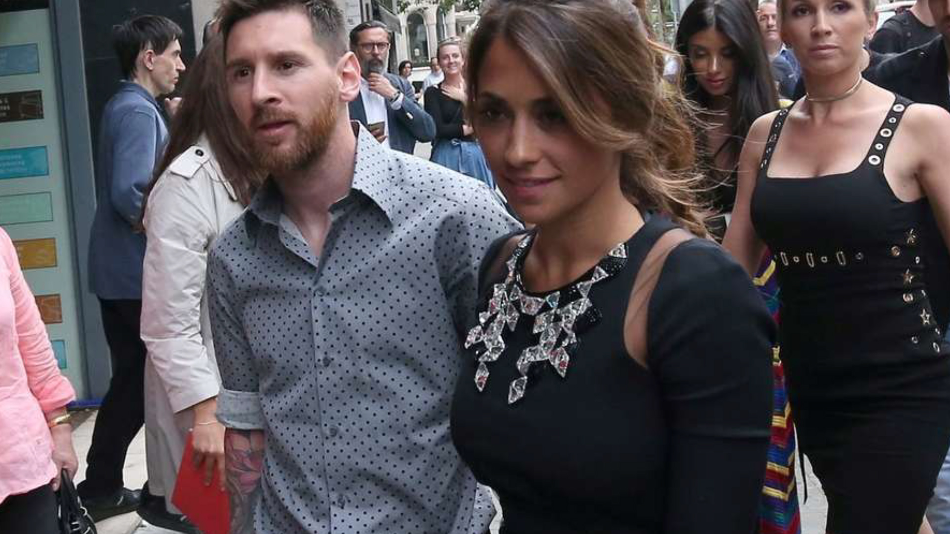 Con look relajado de camisa gris y lunares negros, Messi acompañó en su nuevo proyecto a su mujer, quien lució un vestido streech negro con piedras en el escote (2017 sarkany)