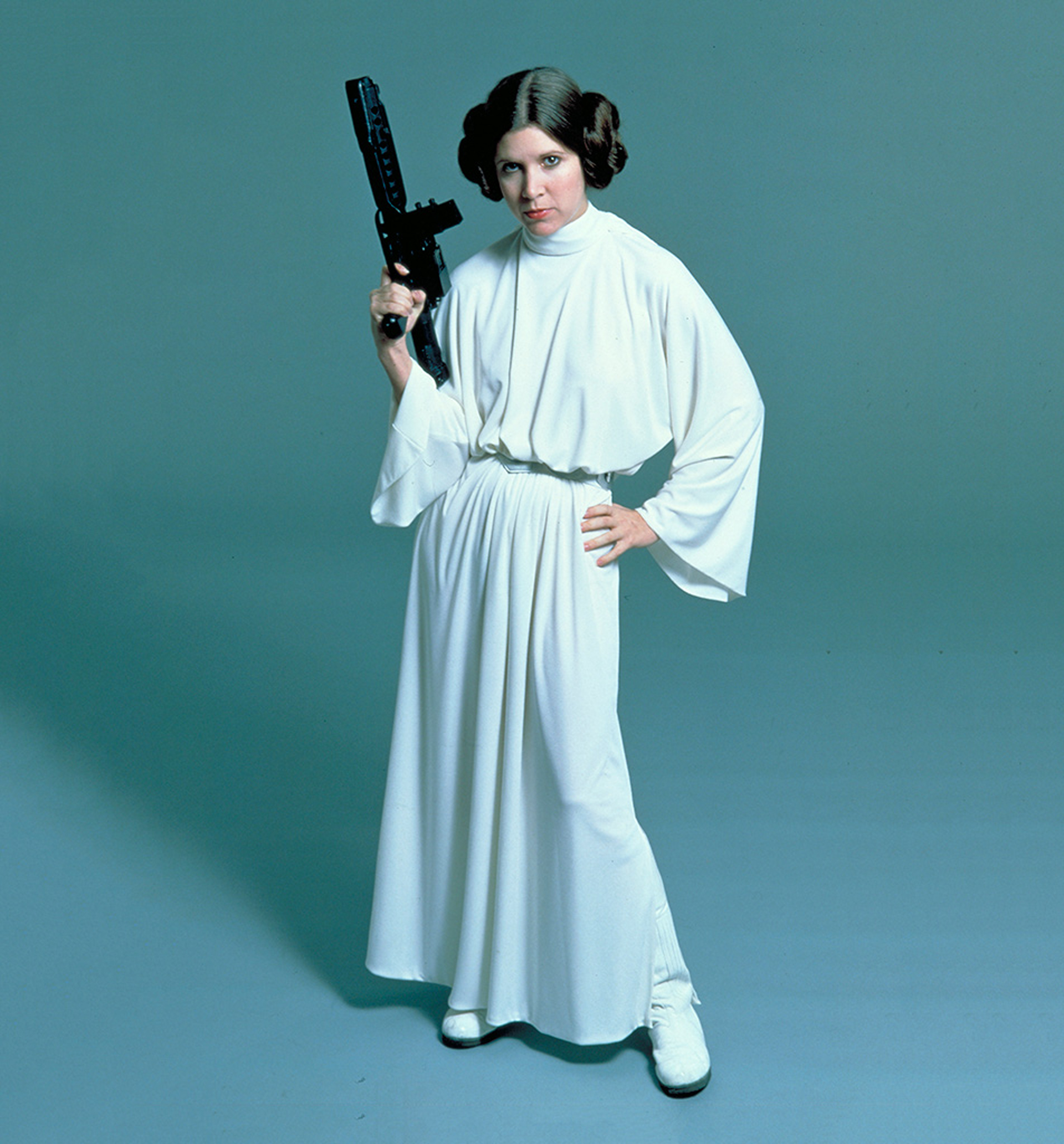 Carrie Fisher como Leia de Star Wars, con una túnica blanca con mangas acampanadas, cuello polera, faja en la cintura y botas blancas