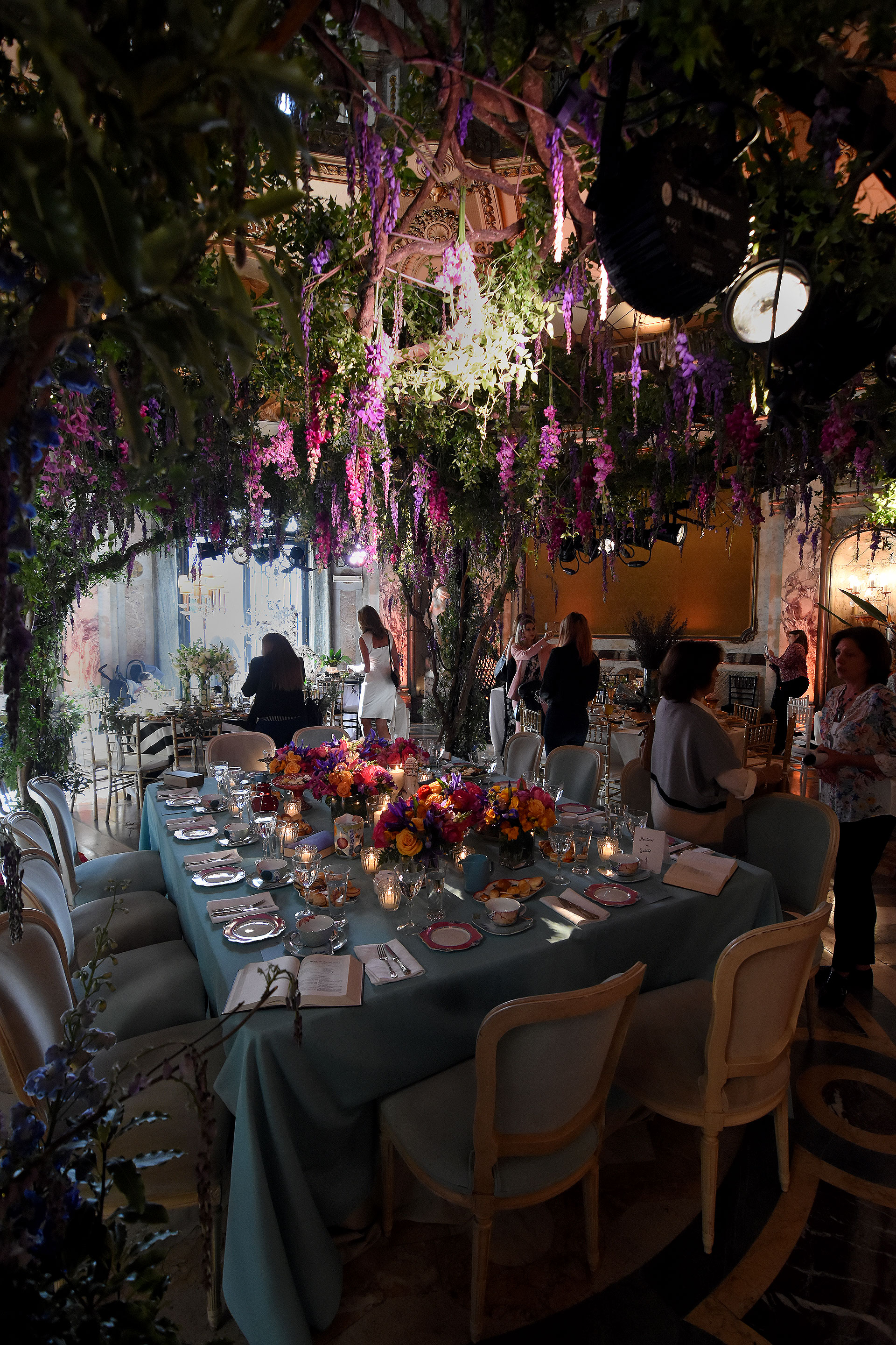 “Momentos con sentido” by Gloria Cesar. Una de las mesas principales entre árboles con flores en caída y centros de mesa con rosas, fresias en amarillo, violeta y rosas. Vajilla de colores y diseños sobre un mantel aguamarina