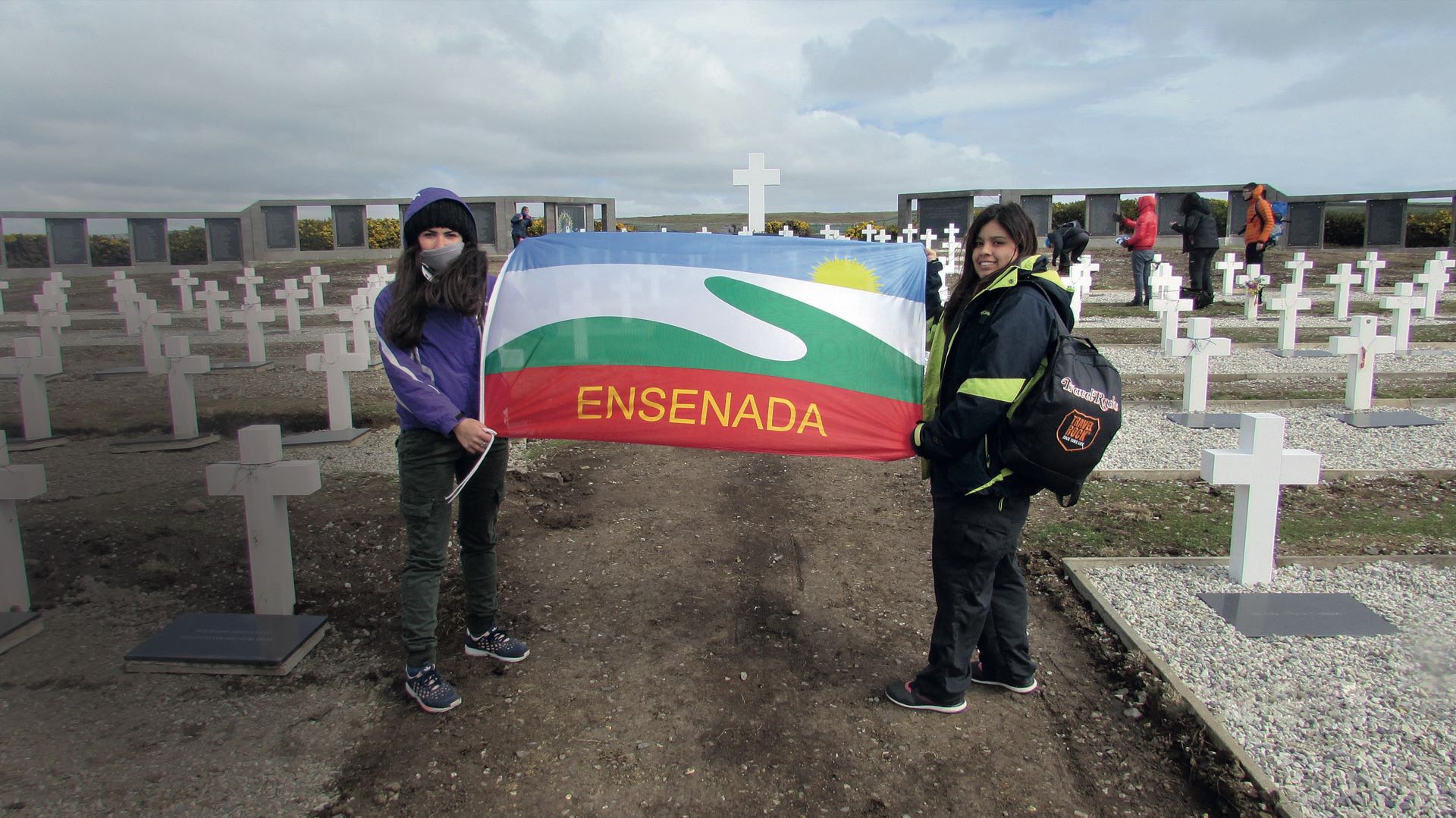 En el cementerio, las alumnas Juana Mosca y Lissete Gauna con la bandera de Ensenada. “Hijos y nietos de ex combatientes estudiaron en nuestra escuela”.