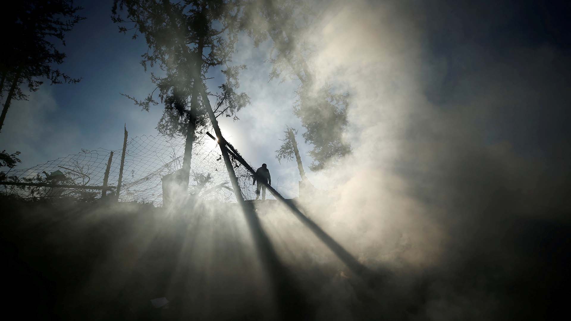 Humo es visto mientras un hombre palestino inspecciona un objetivo militar que fue alcanzado en un ataque aéreo israelí en el norte de la Franja de Gaza el 9 de diciembre de 2017.
