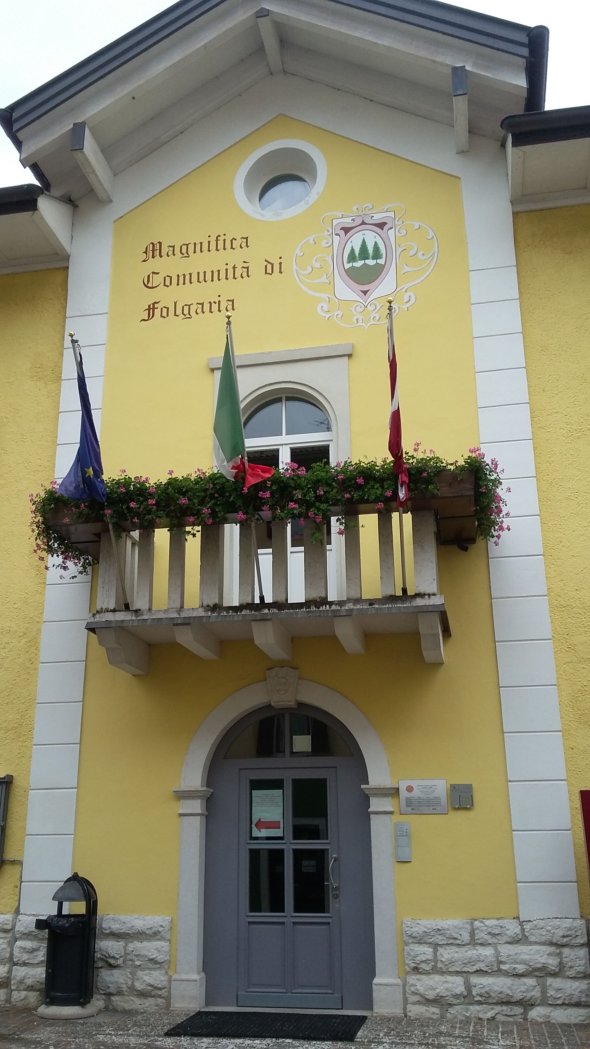La intendencia de la Magnífica Comunidad de Folgaria, pintada íntegramente de amarillo, luce el escudo con tres abetos que identifica a la comuna libre e independiente.