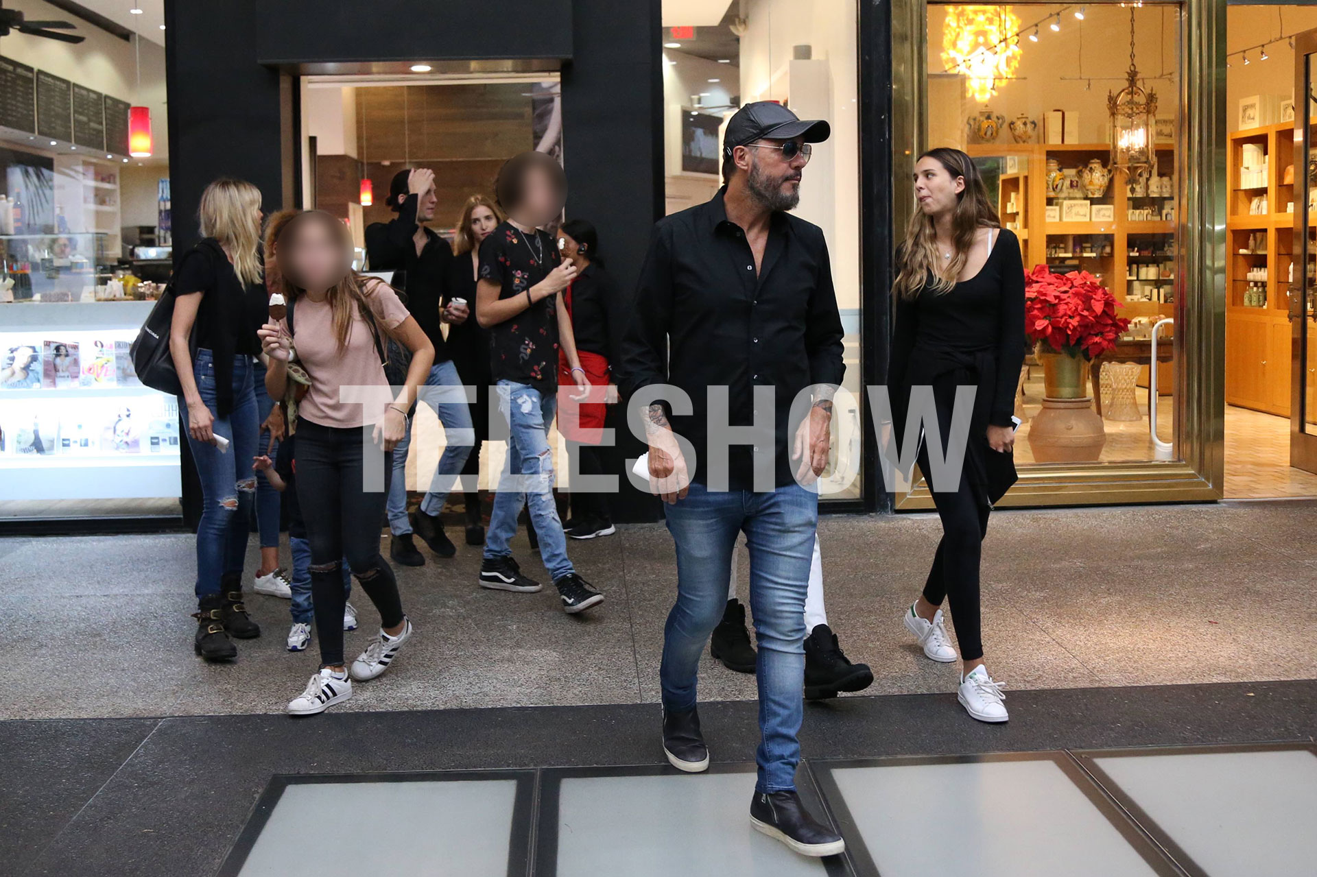 Gorra, anteojos de sol, camisa negra, jeans y zapatillas para Tinelli