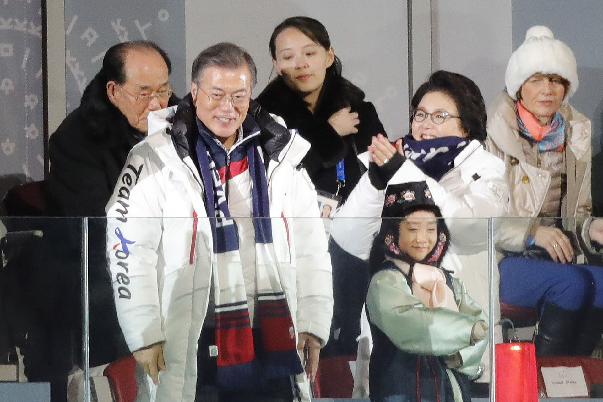 Moon Jae-in sonríe, rodeado de su esposa, Kim Jung-sook (aplaude a su lado) y Kim Yo-Jong, hermana de Kim Jong-un. Detrás suyo, el jefe de la delegación norcoreana, Kim Yong-nam
