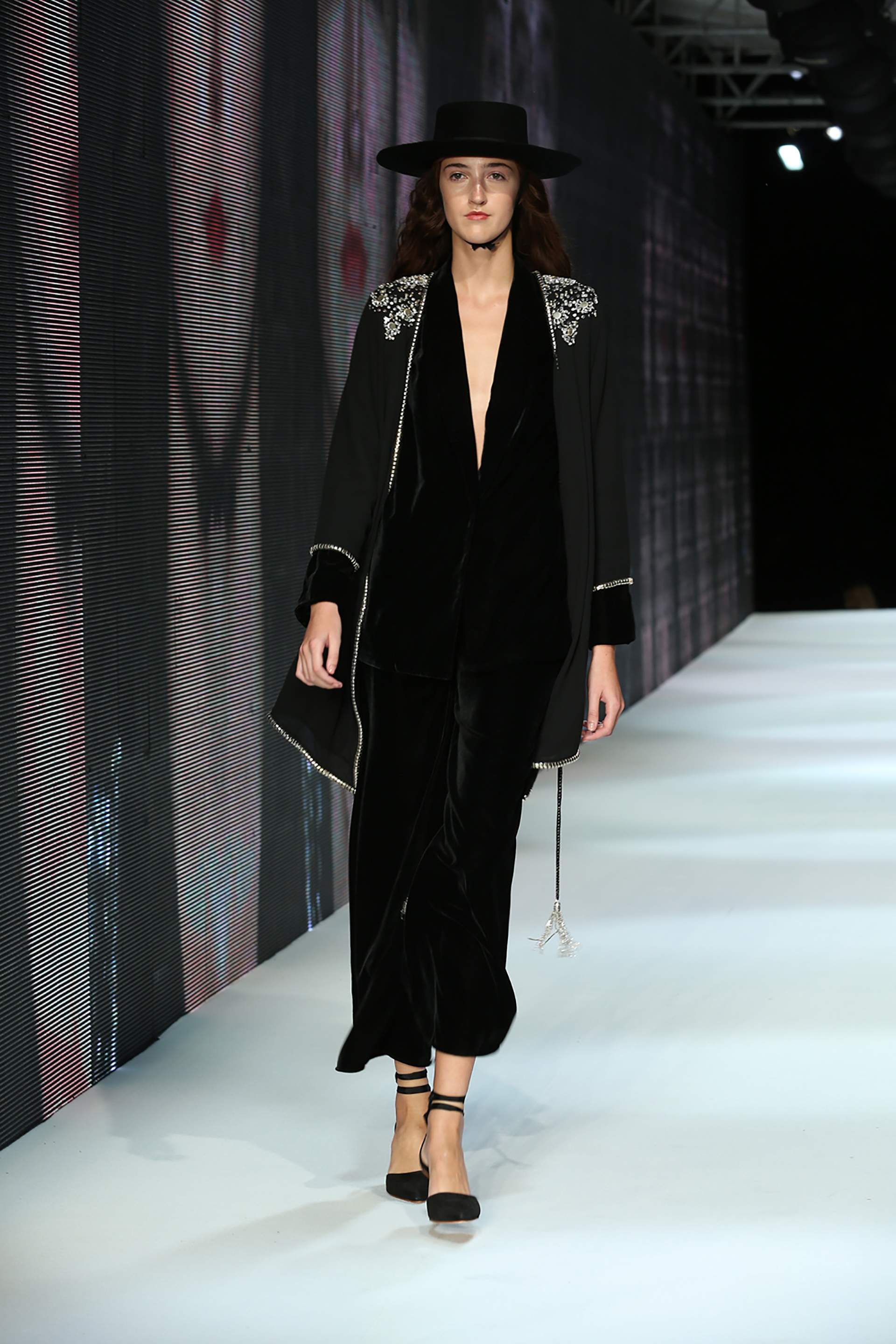 Conjunto de pantalón y saco en chiffon negro acompañado de una bata con detalles de puño en terciopelo y envivado de piedras con bordado plateado en los hombros. Su propuesta es romántica y naïf, reflejando la simpleza y pulcredad sin perder el encanto de una mujer excitante y apasionada