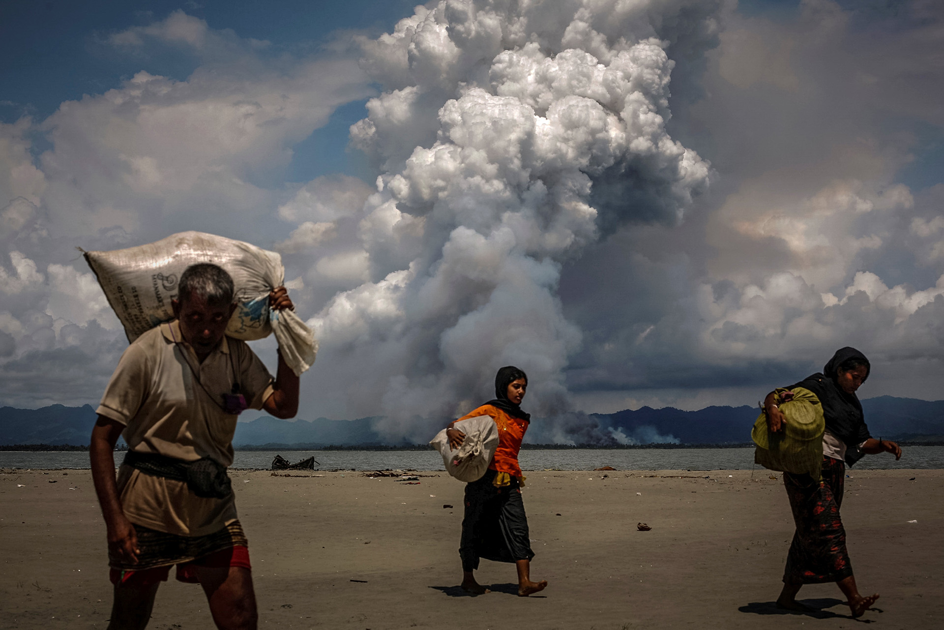 Se ve humo en la frontera de Myanmar cuando los refugiados rohingya caminan por la orilla después de cruzar la frontera entre Bangladesh y Myanmar en barco por la Bahía de Bengala, en Shah Porir Dwip, Bangladesh, el 11 de septiembre de 2017. (Danish Siddiqui)