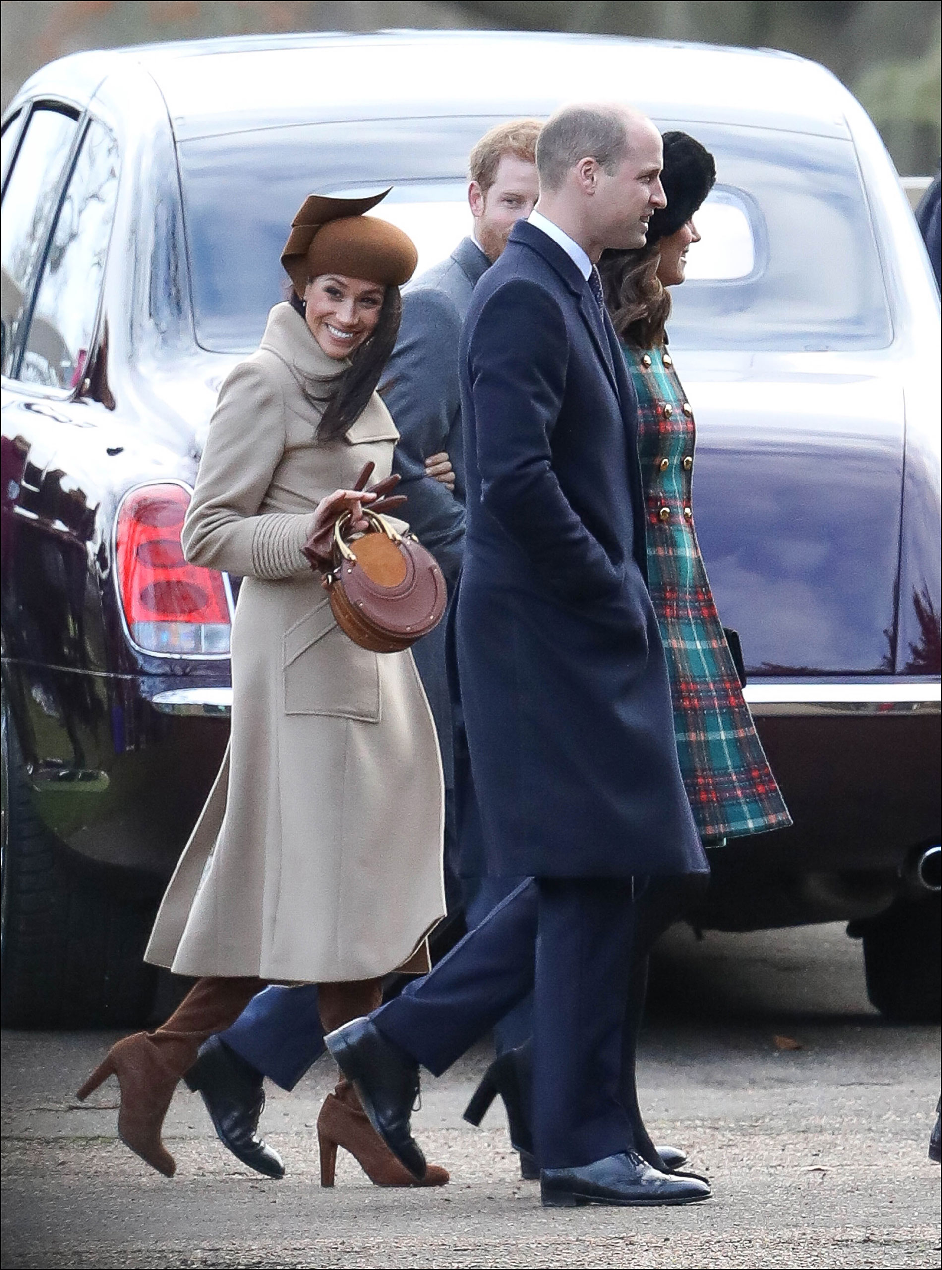 Meghan sonriente en tonos marrones: Botas de caña alta, tapado largo, tocado y mini cartera.