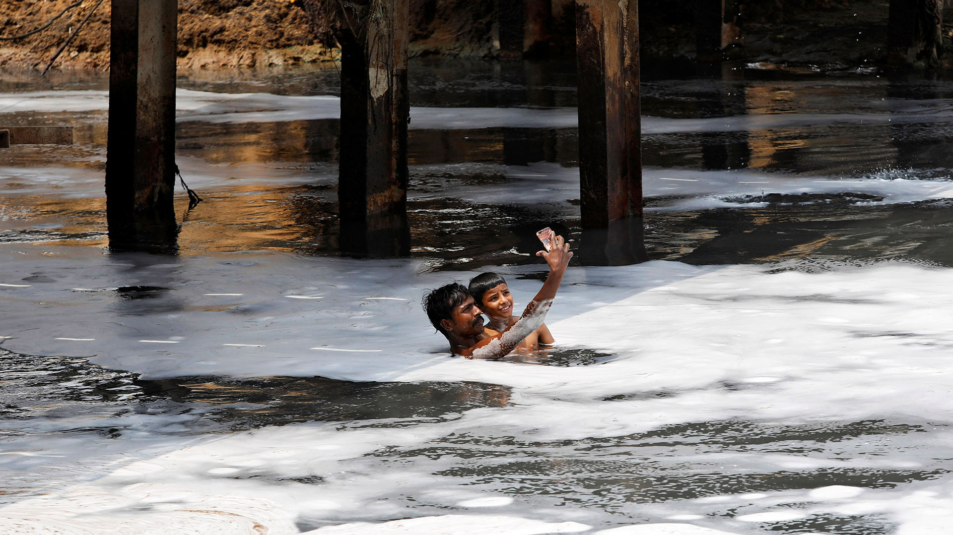 Un hombre y un niño sonríen para una foto mientras nadan en las contaminadas aguas del Río Yamuna en Nueva Delhi, India (REUTERS/Saumya Khandelwal)