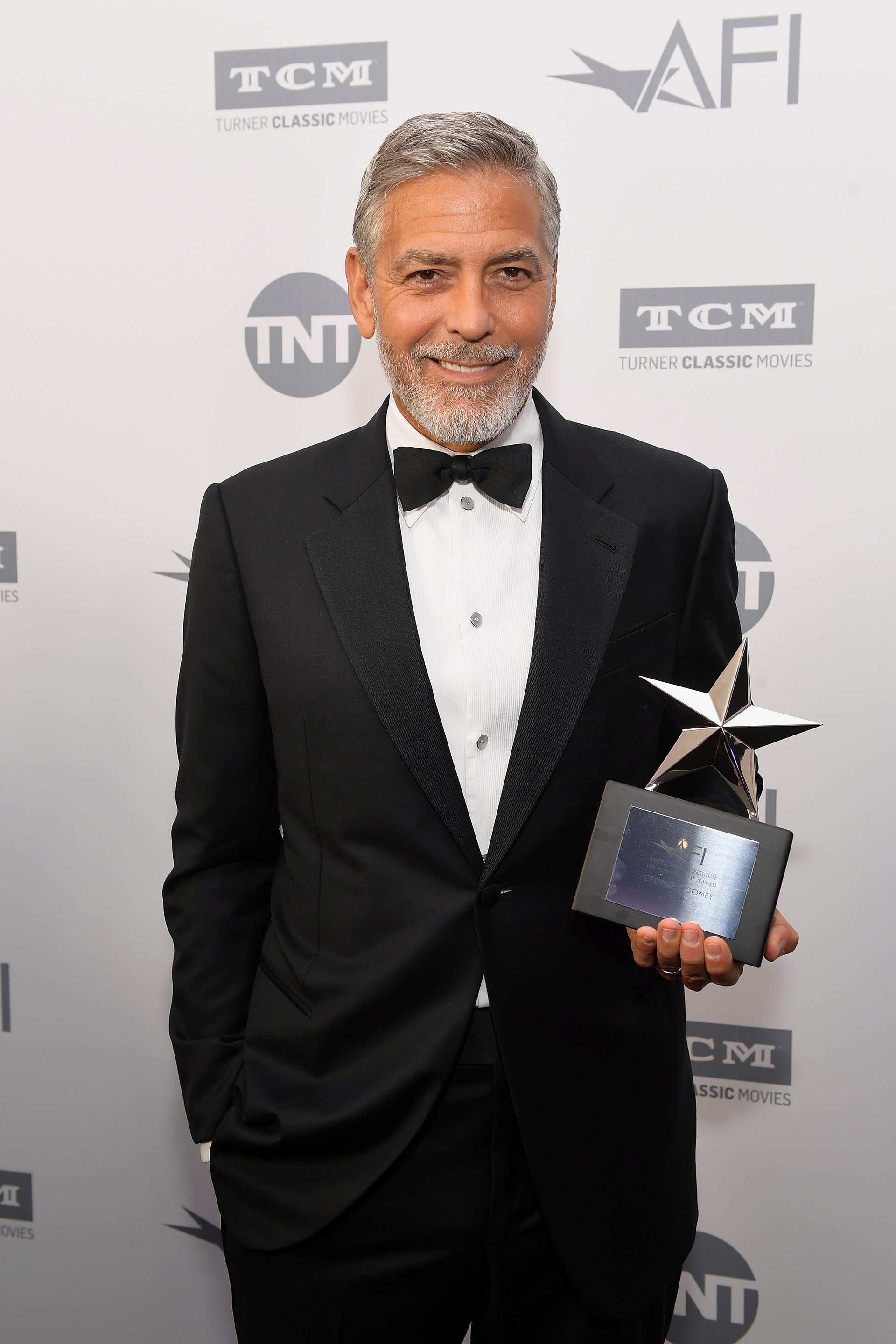 Vestido con un elegante smoking, George Clooney posa con su premio