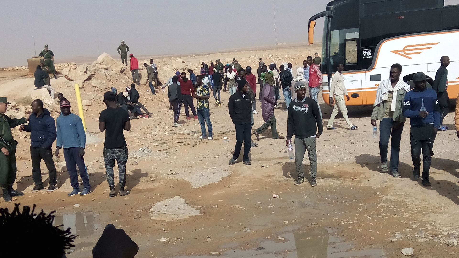 Un grupo de migrantes espera la deportación mientras es vigilado por soldados argelinos (AP)