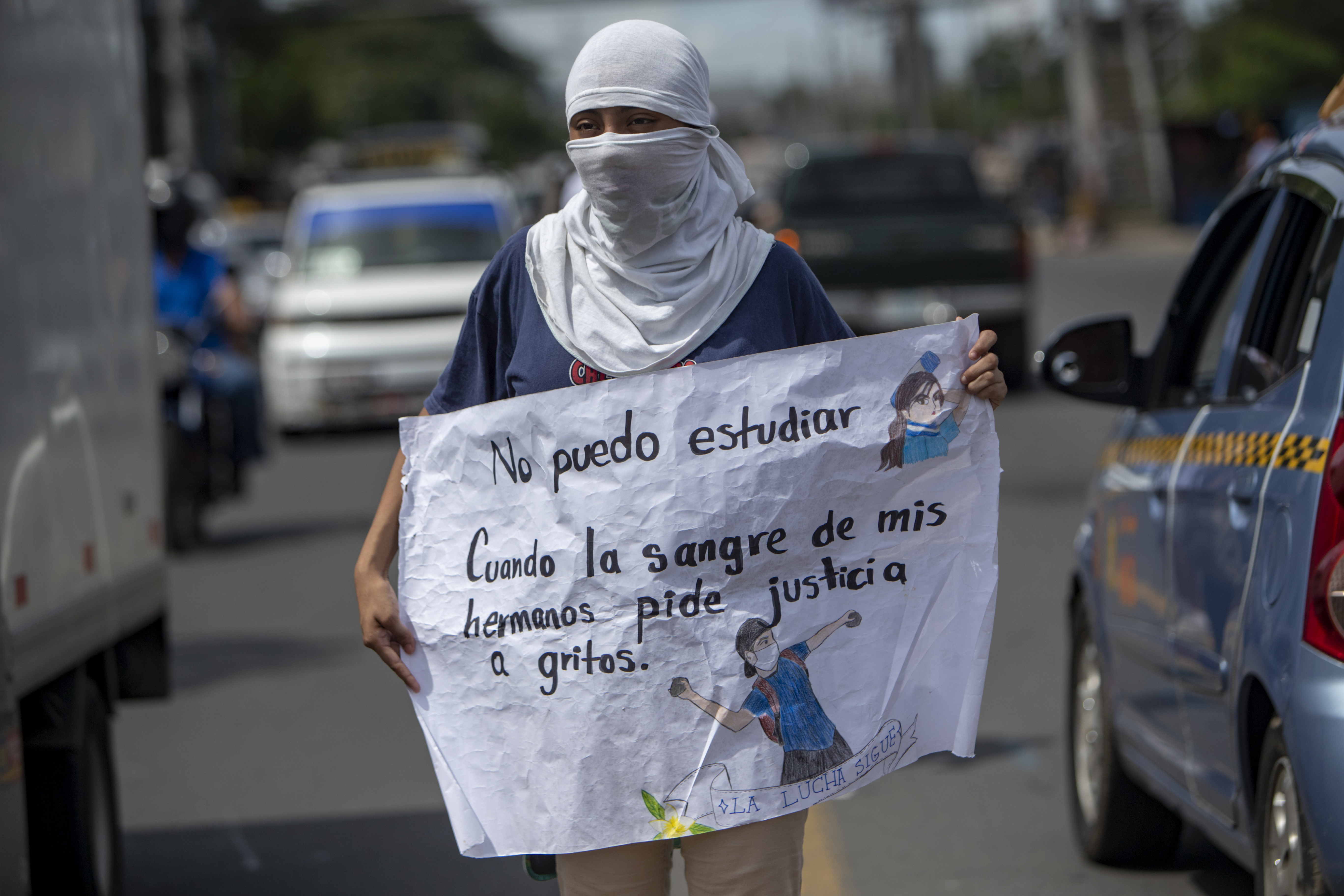 Una joven con la cara tapada y un cartel participa de un plantón frente a la Universidad Centroamericana (UCA). (EFE/Jorge Torres)