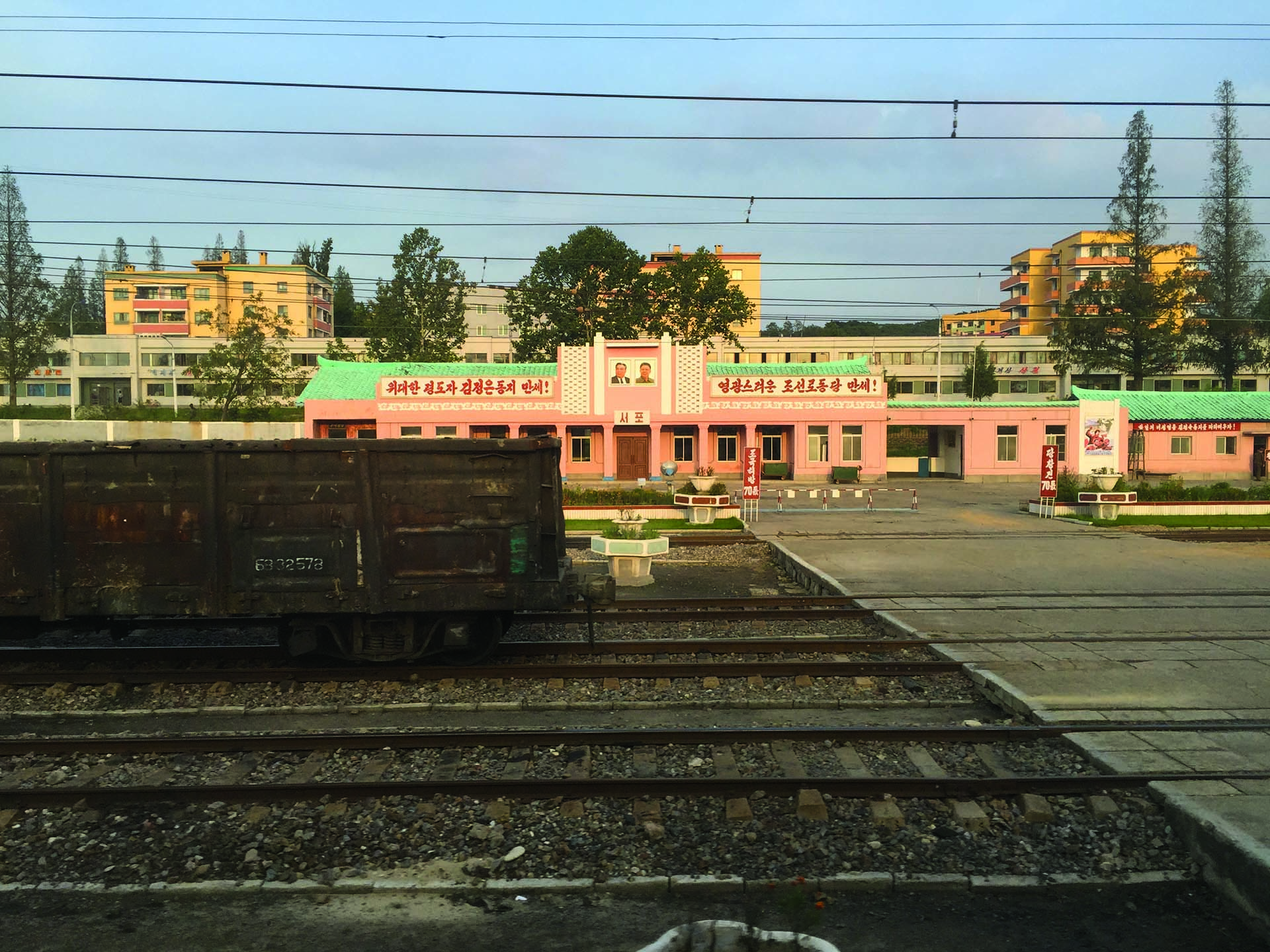 Llegué a Pyongyang desde Pekín en un viaje en tren que duró un día entero. Poco después de atravesar la frontera, el tren aminoró la velocidad y se detuvo en una estación que podría haber pasado perfectamente por un hotel rural o un hospital pequeño. Entonces di un salto, corrí hasta una de las ventanillas del pasillo y filmé mi primer video norcoreano en cámara lenta. Los retratos de los Kim sonreían desde la entrada; era oficial, estábamos en Corea del Norte. En los carteles se lee: “¡Viva nuestro gran líder Kim Jong Un!” (izq.) “¡Viva el glorioso Partido de los Trabajadores!” (der.)