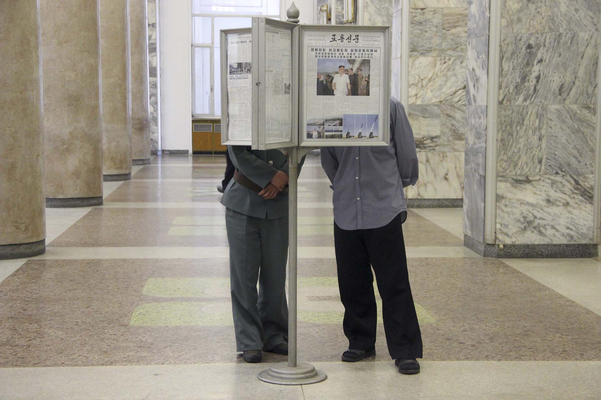 Dos hombres leen en vitrina el periódico oficial, Rodong Sinmun, con Kim Jong Un en la portada. Desde que llegó al poder, el tercer Kim se transformó en una reencarnación moderna de su abuelo y aumentó de peso para acentuar su parecido natural hasta encarnar el nuevo ideal masculino de éxito: la gordura. Aunque ya no hay hambrunas en Corea del Norte, la mala nutrición sigue siendo generalizada en el interior y la prosperidad se mide, también, en kilos