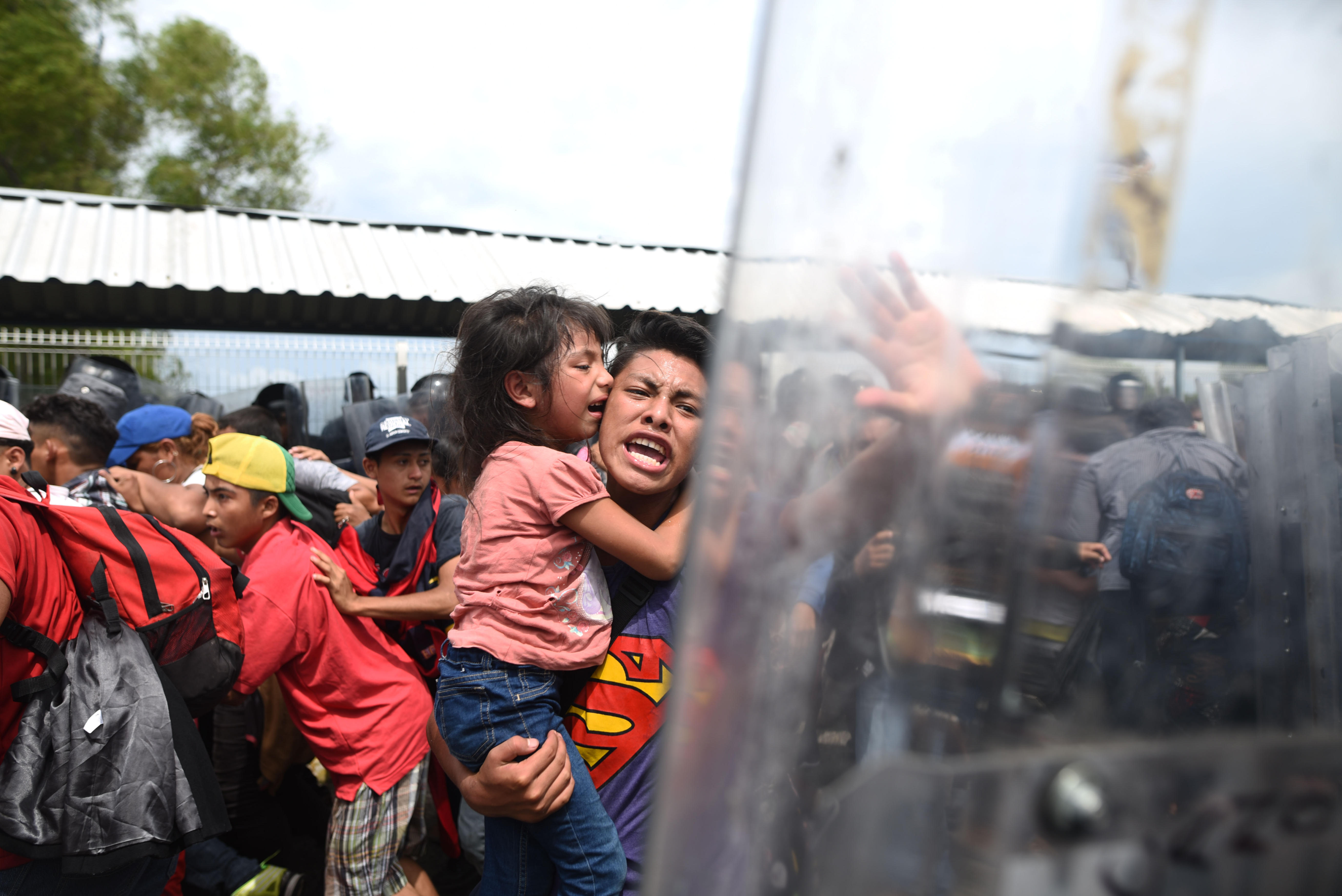 Un migrante hondureño con una menor en brazos grita hacia los miembros de la policía mexicana en el paso fronterizo entre Guatemala y México. (EFE/Edwin Bercían)