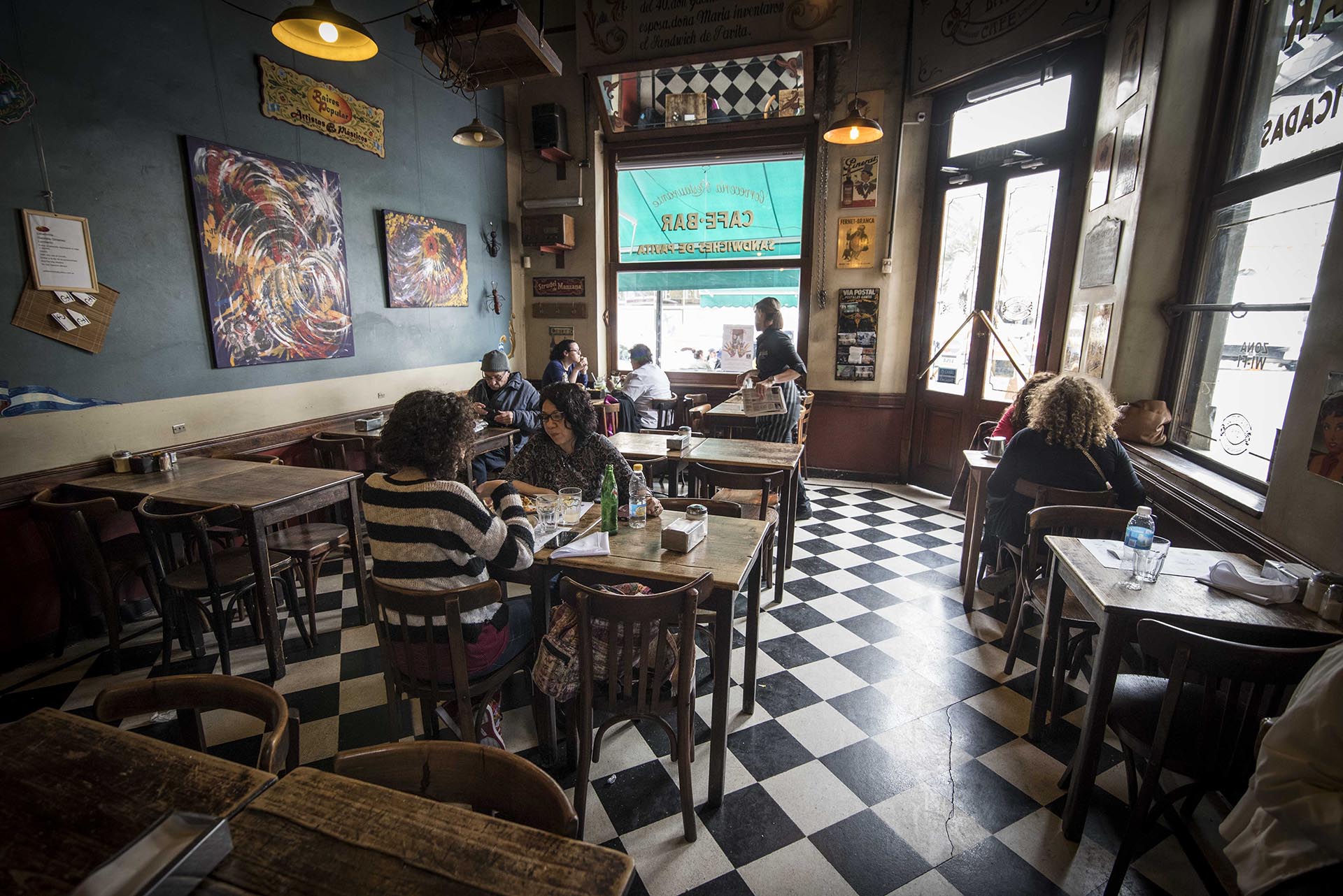 Piso blanco y negro, con mesas y sillas de madera, un café clásico del barrio