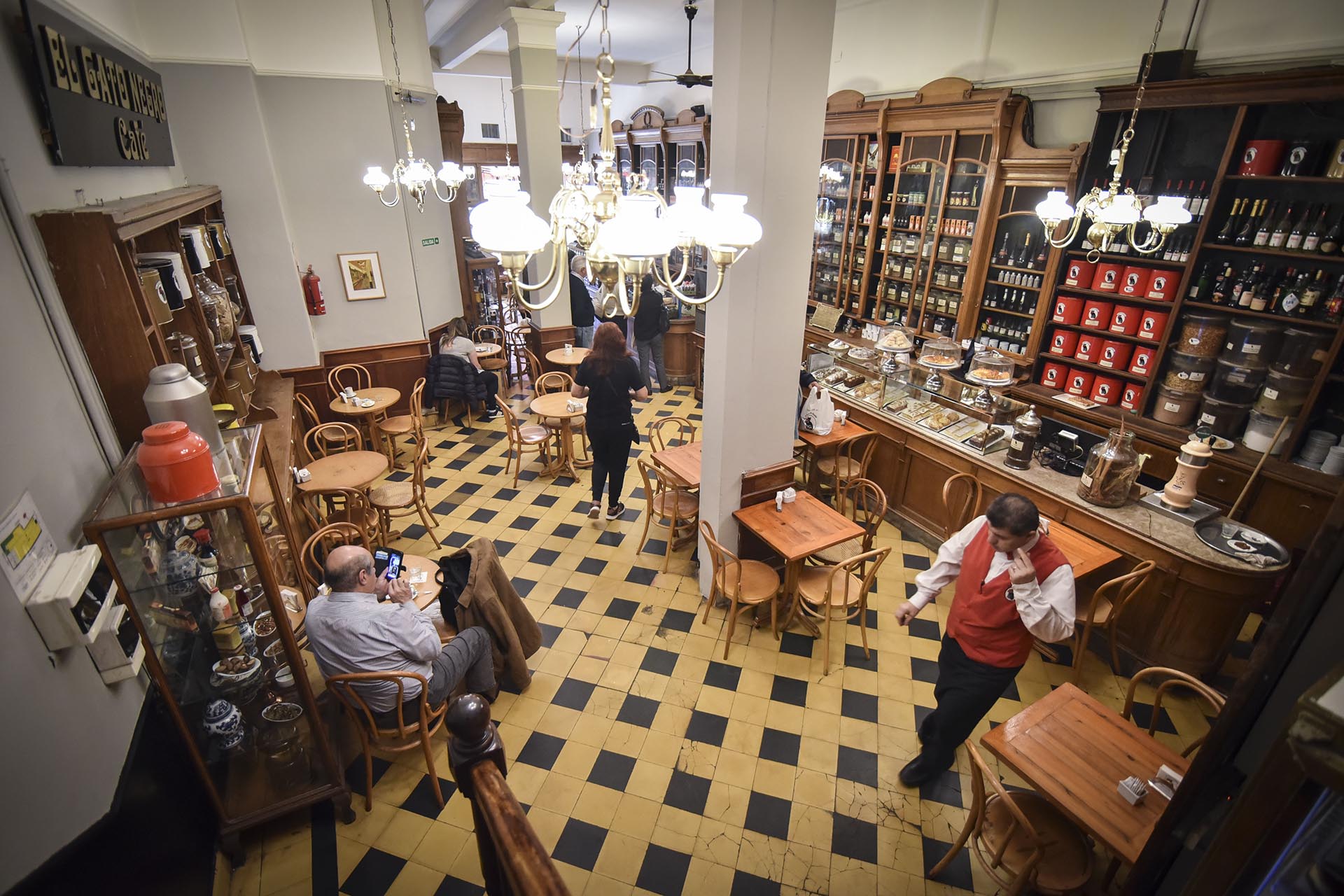 Desde la escalera de El Gato Negro. Piso cuadrillé en amarillo y negro, mesas y sillas de madera, un ícono del bar