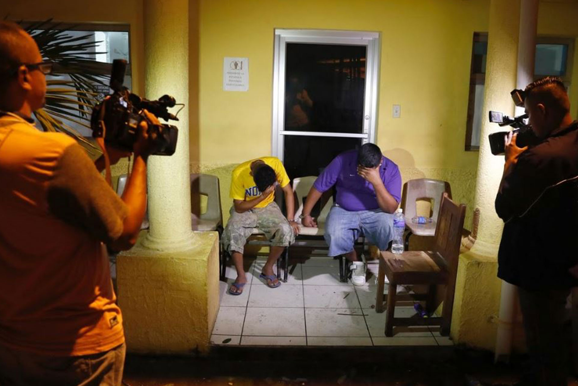 Dos personas se cubren sus rostros mientras son filmados por cámaras