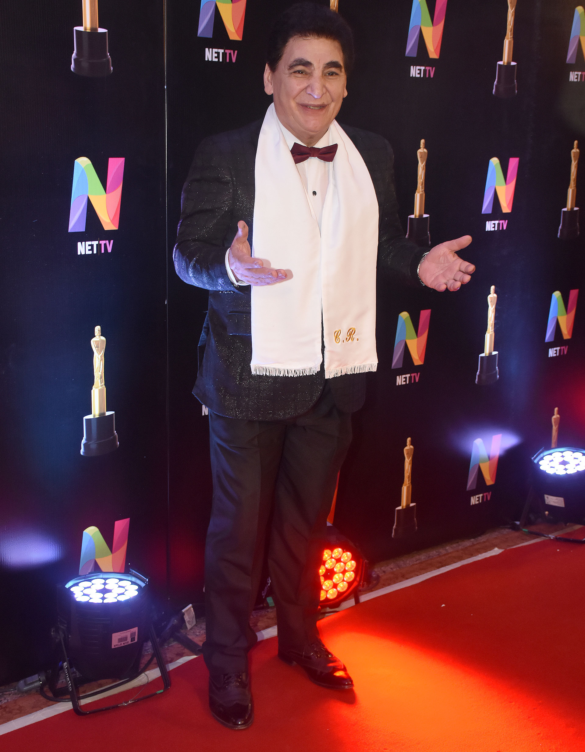 Cacho Rubio fiel a su chalina blanca, completó el su look con un traje de saco con brillos a cuadros, pantalón negro, zapatos de cuero combinado con charol y moño bordó