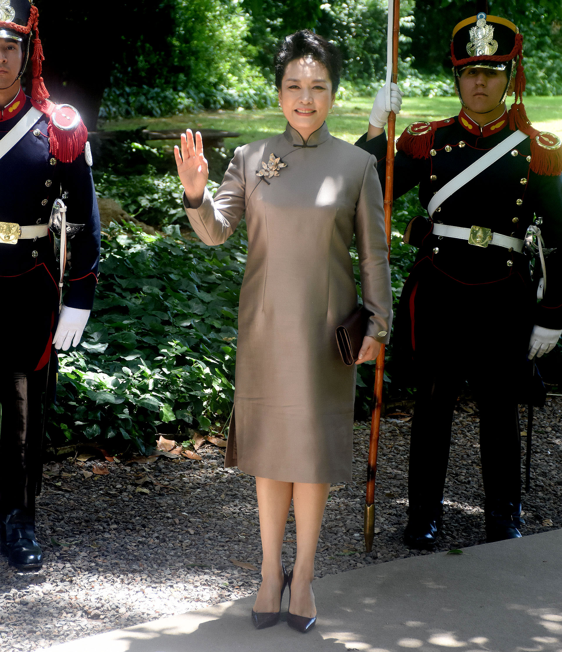 Liyuan Peng, la primera dama de China lució un quipao, la vestimenta tradicional del país en gris plomo con detalle de broche-joya sobre el vestido. Lo acompañó con un sobre y stilettos en punta marrón