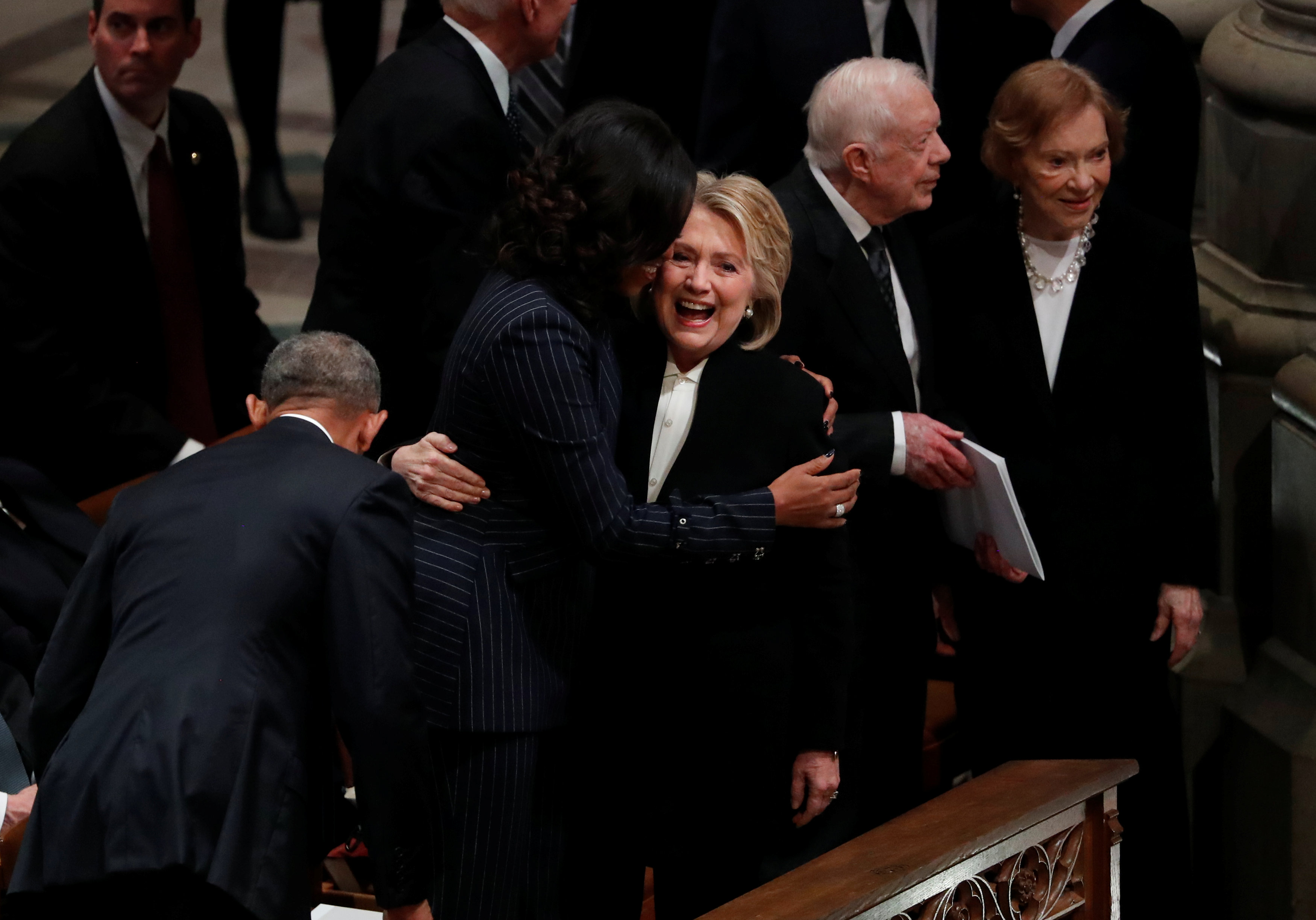 La ex secretaria de Estado de Estados Unidos Hillary Clinton abraza a la ex primera dama Michelle Obama frente al ex presidente Jimmy Carter y a la ex primera dama Rosalynn Carter en el funeral de estado del ex presidente George H.W. Bush en la Catedral Nacional de Washington en Washington, Estados Unidos, el 5 de diciembre de 2018. (Reuters)