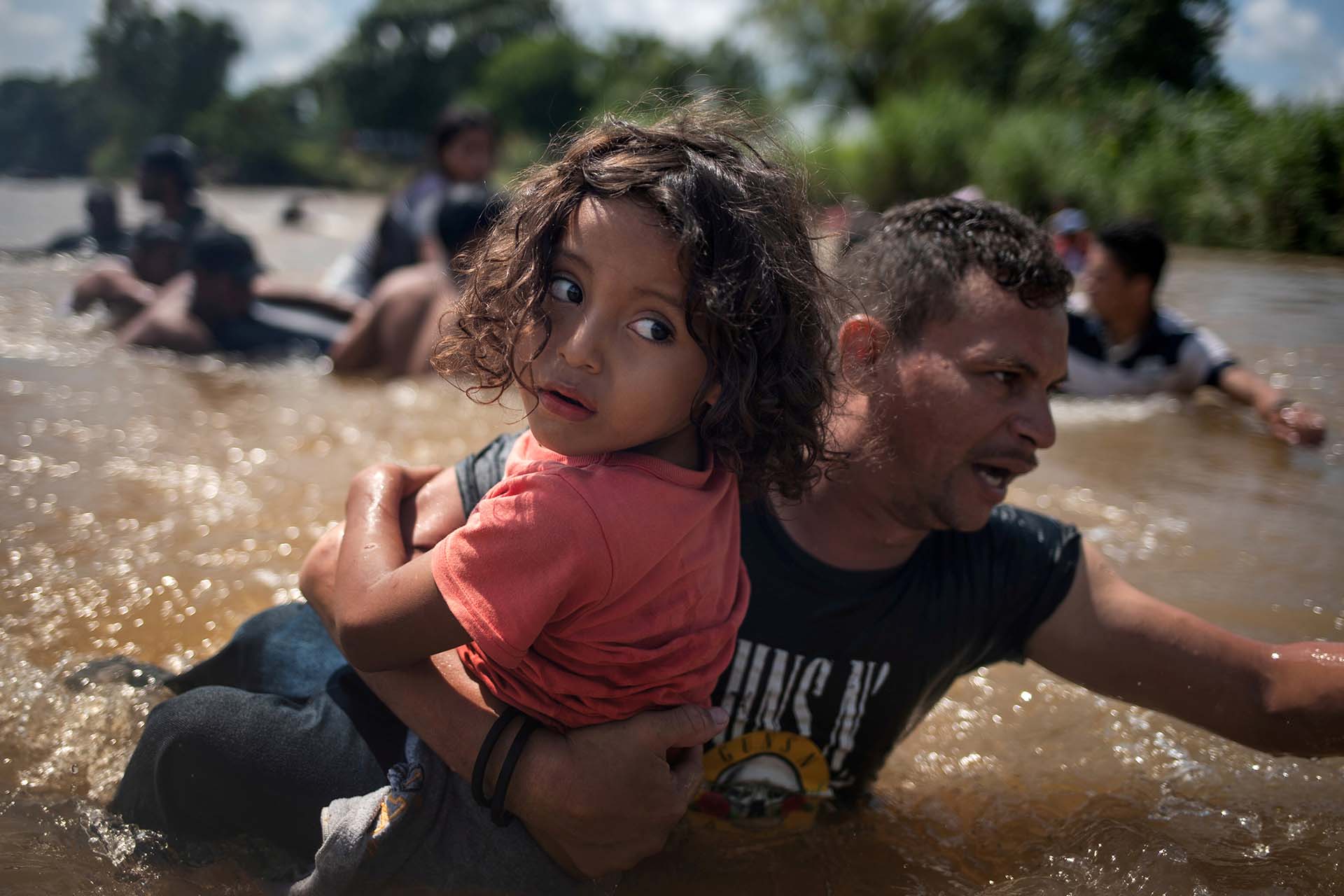 Luis Acosta sostiene como puede al pequeño Ángel Jesús, de 5 años. Ambos son de Honduras e intentan cruzar el río Suchiate a México desde Guatemala, el 29 de octubre, con el objetivo final de llegar a los EEUU