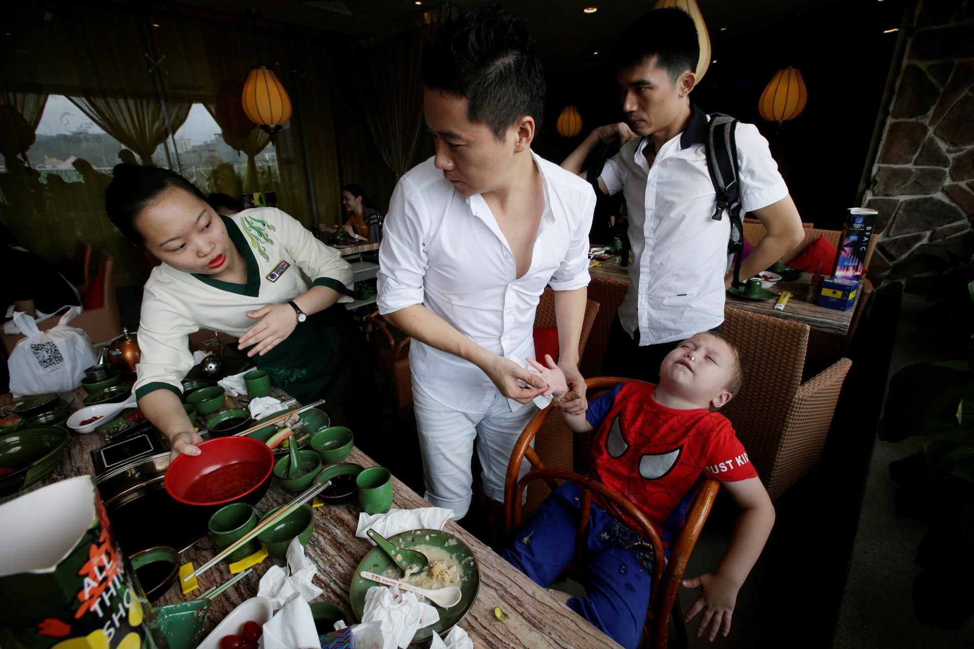 Un camarero ayuda a An Hui y su compañero Ye Jianbin con uno de sus hijos. An Zhiya sufre una hemorragia nasal después de un almuerzo en un restaurante en Shenzhen, provincia de Guangdong, China, el 17 de septiembre de 2018.