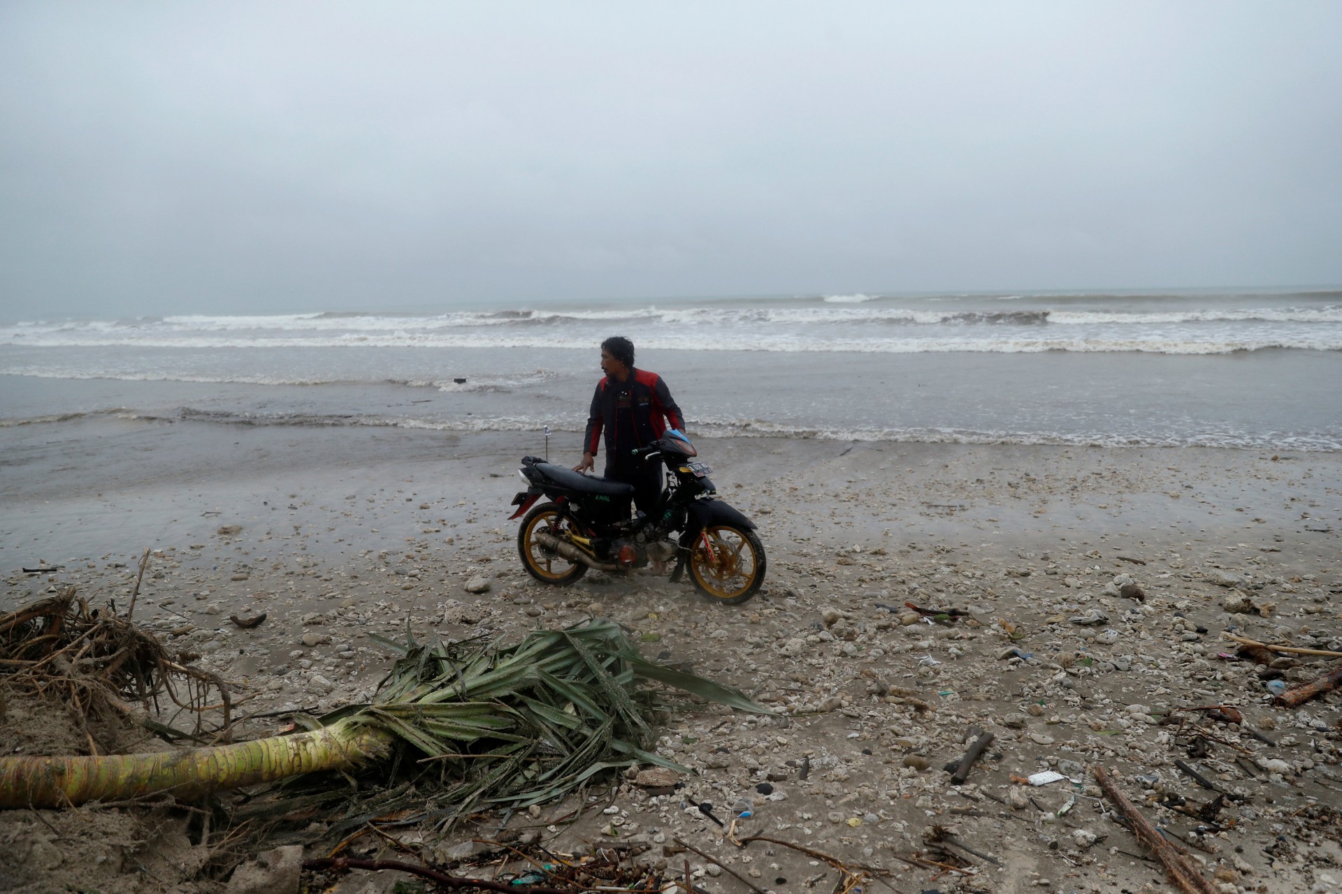 Un hombre está parado junto a una motocicleta en una playa azotada por un tsunami, cerca de Sumur, provincia de Banten, Indonesia, 26 de diciembre de 2018.