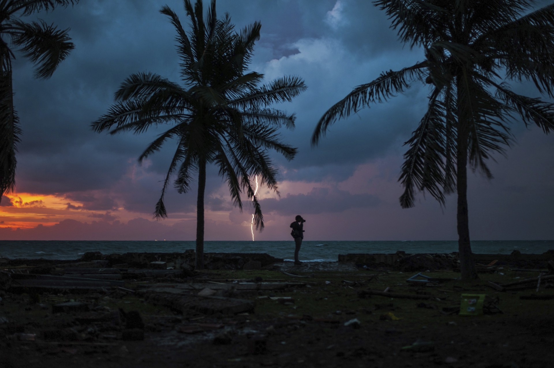 La puesta de sol siluetea a un reportero gráfico con un rayo en un centro turístico afectado por el tsunami del sábado en Indonesia, el martes 25 de diciembre de 2018.