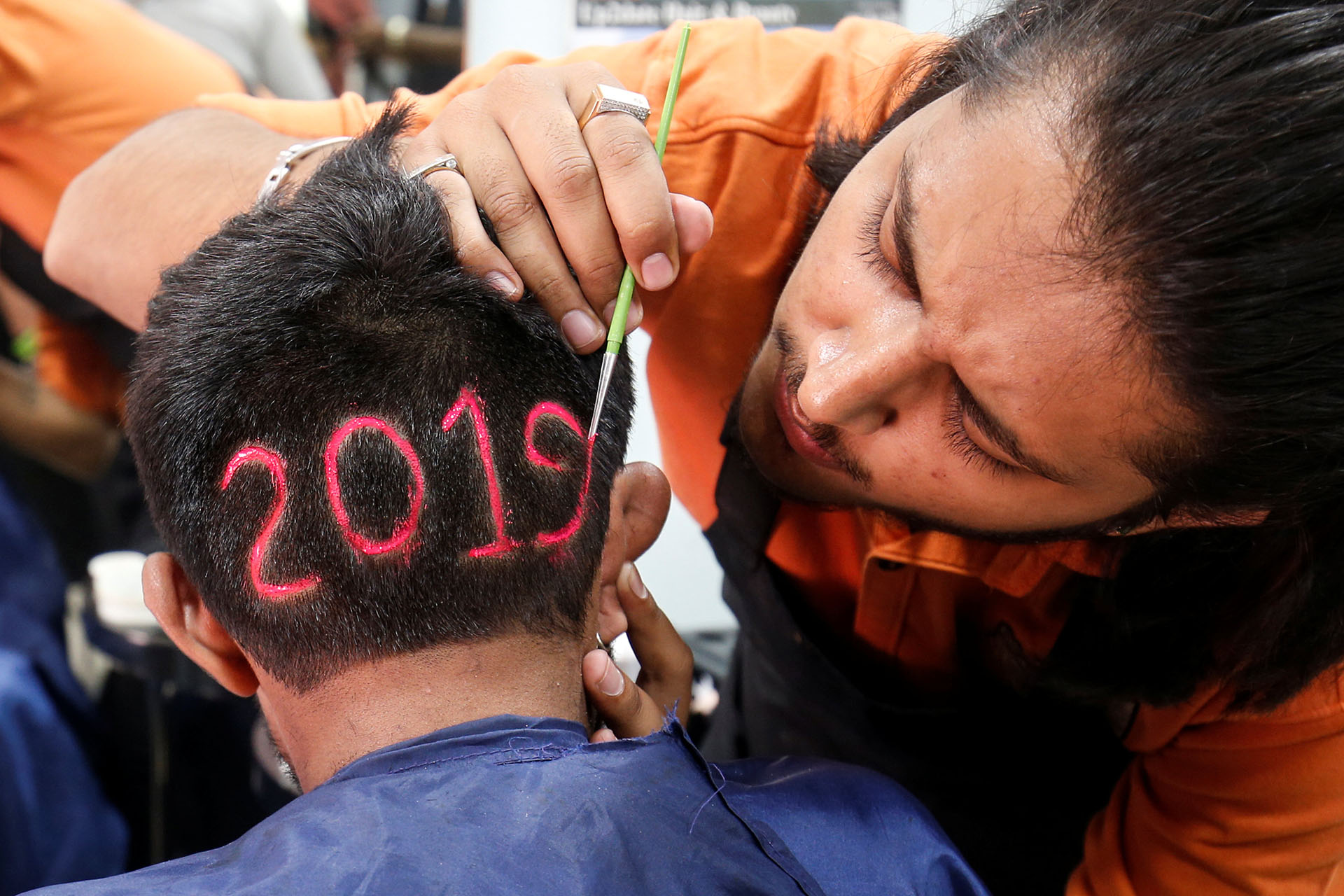 Un peluquero trabaja sobre la cabeza de su cliente en una barbería de Ahmedabad, India