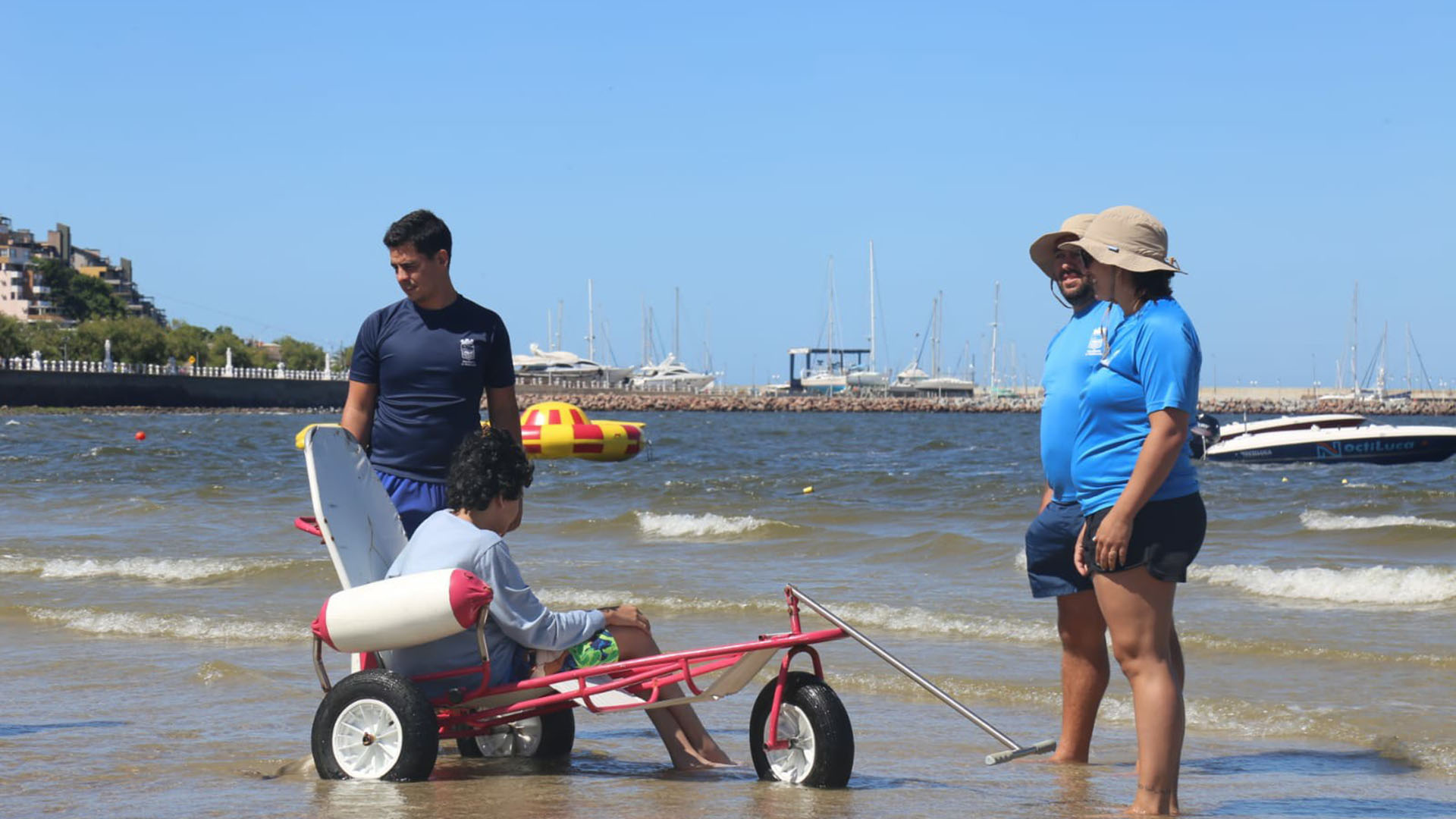 La silla, el joven y los profesionales encargados de llevarlo al agua: una postal de la playa inclusiva