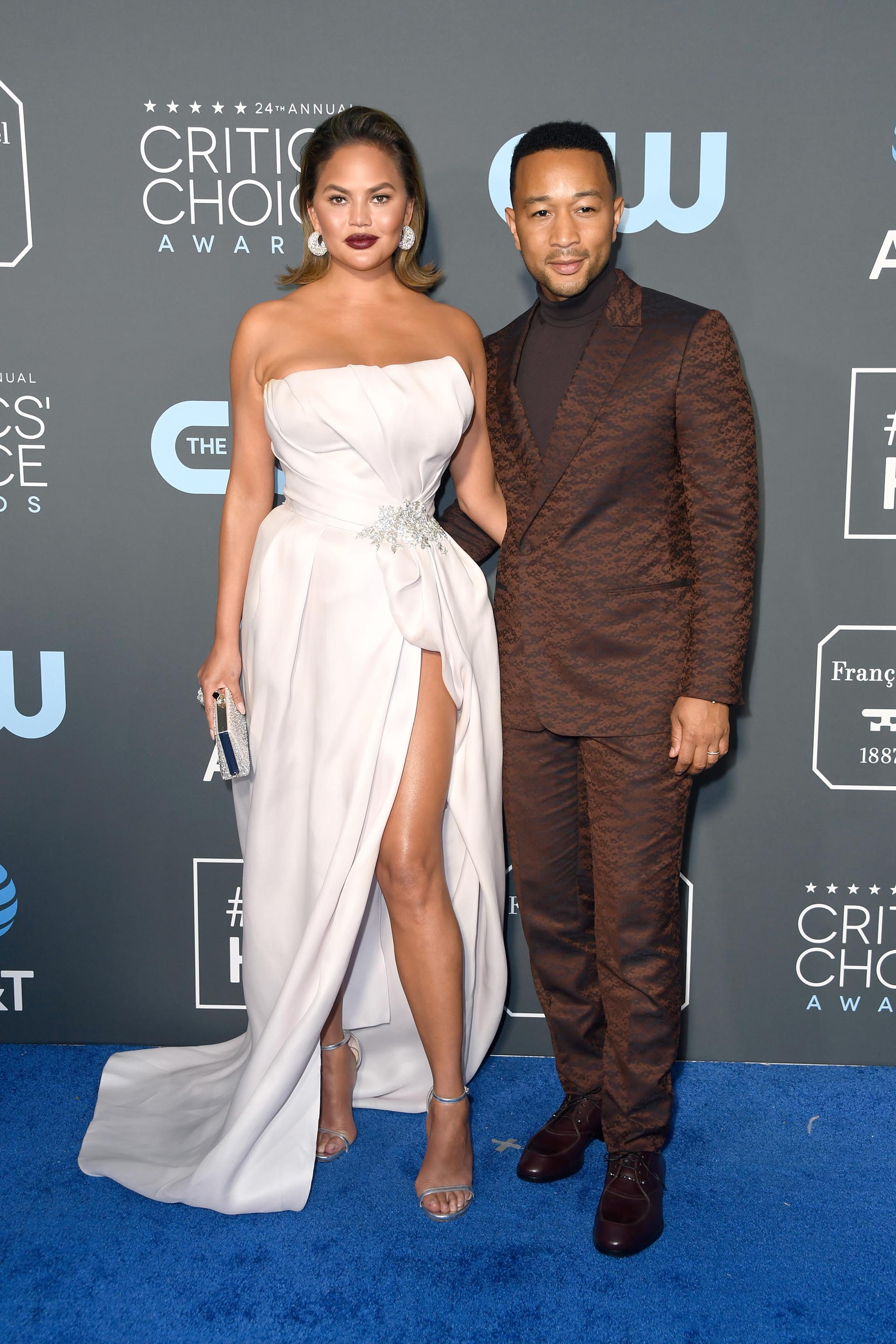 Chrissy Teigen y John Legend. El cantante apostó a un look extravagante con un esmoquin tramado en animal print marrón, zapatos acordonados de cuero a tono y polera también en color marrón. La modelo eligió un diseño strapless drapeado con detalle de gran broche en el costado y tajo profundo. Completó el look con sandalias plateadas y clutch rígido