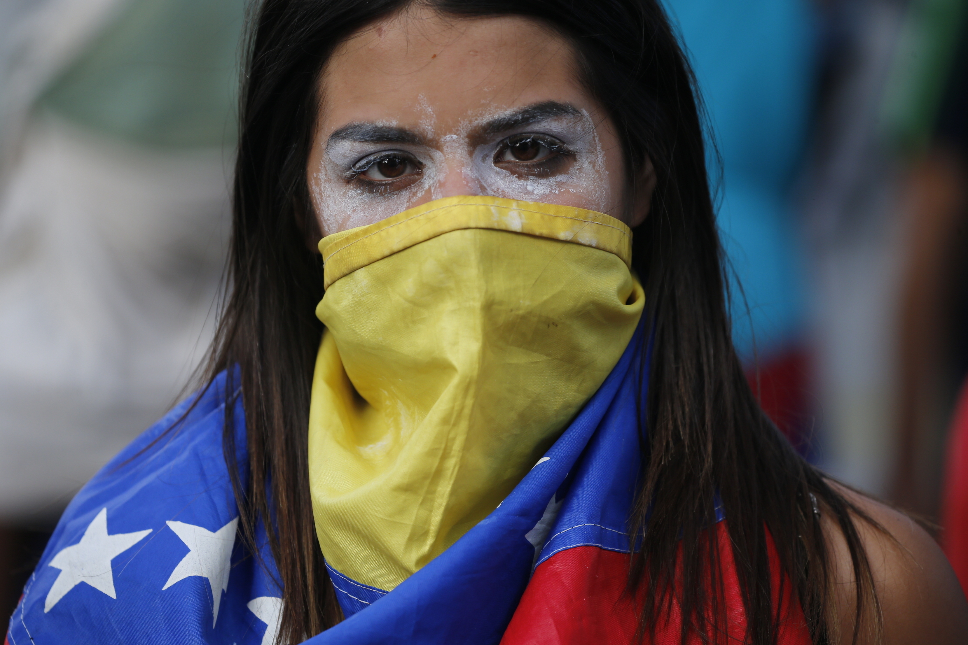 Una manifestante antigubernamental, con la cara tapada por una bandera de Venezuela y pasta dentífrica alrededor de los ojos para mitigar el efecto de los gases lacrimógenos, durante enfrentamiento con las fuerzas de seguridad tras una protesta para exigir la renuncia del presidente del país, Nicolás Maduro, en Caracas, Venezuela, el 23 de enero de 2019. (AP Foto/Fernando Llano)